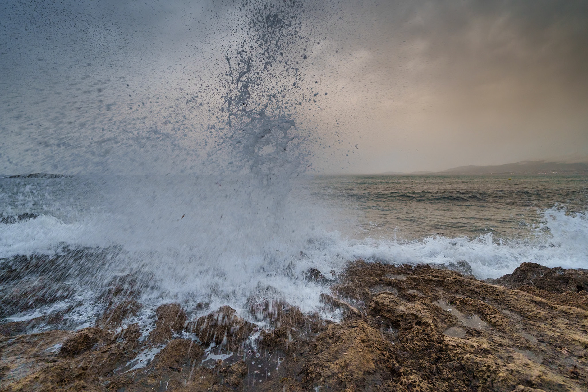 at the shore of coll en rabassa in mallorca, the sea roars its ancient language. a crescendo rises as a wave hurls itself against the stoic rocks, bursting into a thousand droplets like a symphony's climax. the spray reaches skyward, as if to touch the brooding clouds, leaving tales of its journey in the salty mist. the tumultuous grey sky watches over, a canvas to the ocean's fierce performance. here, nature's raw power is on display, a dialogue between the elements, a dance of water and air, energy and stillness, captured in a snapshot of elemental fury.