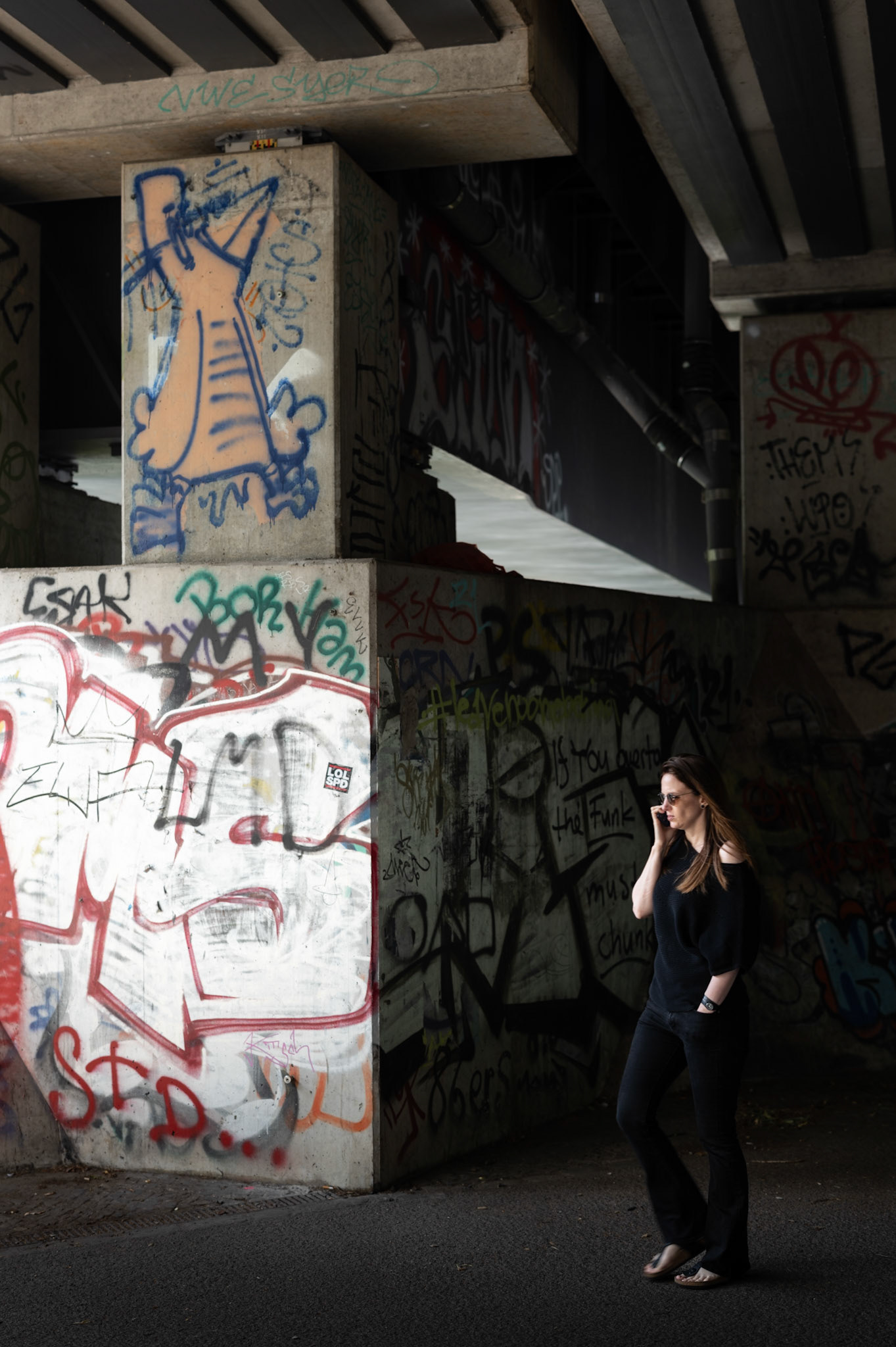 beneath the concrete canopy, a woman strides confidently through the urban underbelly of berlin tiergarten, near the haus der kulturen der welt. the pillars, adorned with vibrant graffiti, stand as silent witnesses to the stories and expressions of the city's unseen artists. her determined walk and the stark contrast of light and shadow reflect the dynamic interplay of culture and modernity in this hidden corner of the metropolis.