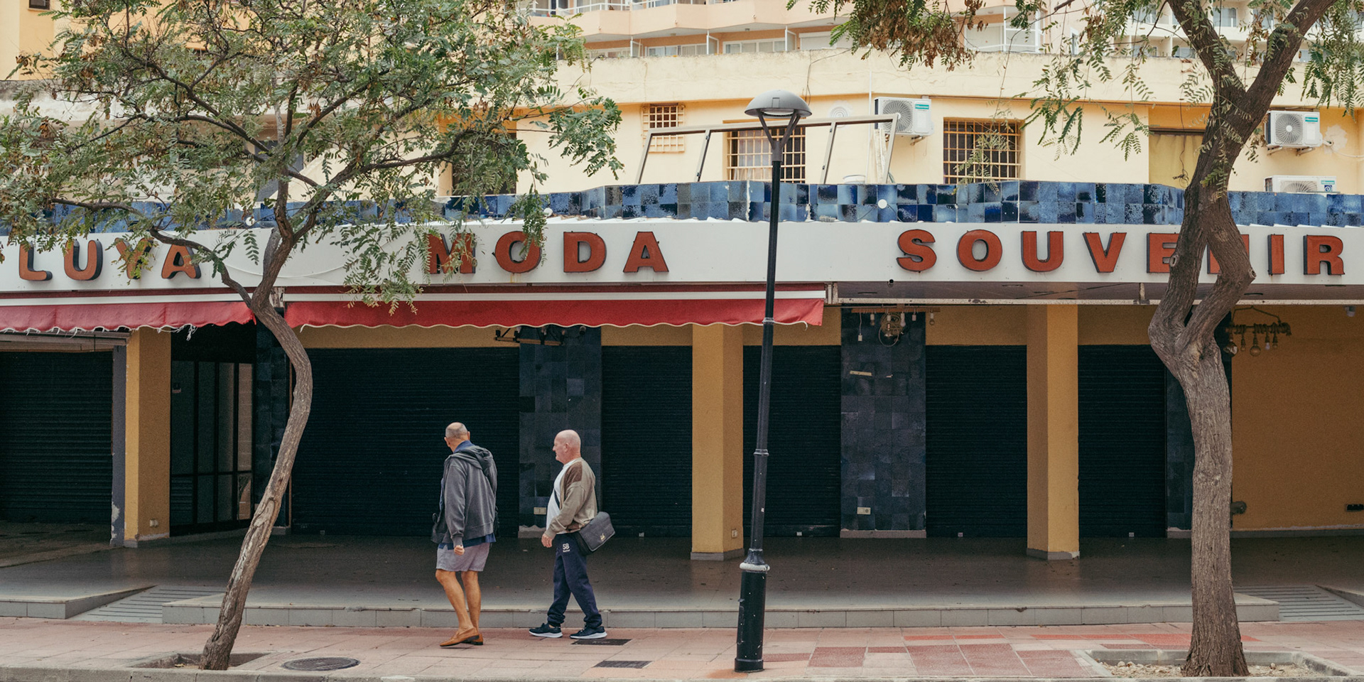in palmanova, winter brings a hush, leaving only a few tourists to tread the quiet streets. the shutters of restaurants and stores are closed for a seasonal pause, echoing the calm. two figures walk past, embodying the tranquil atmosphere of a town at rest, waiting to awaken with the return of summer visitors.