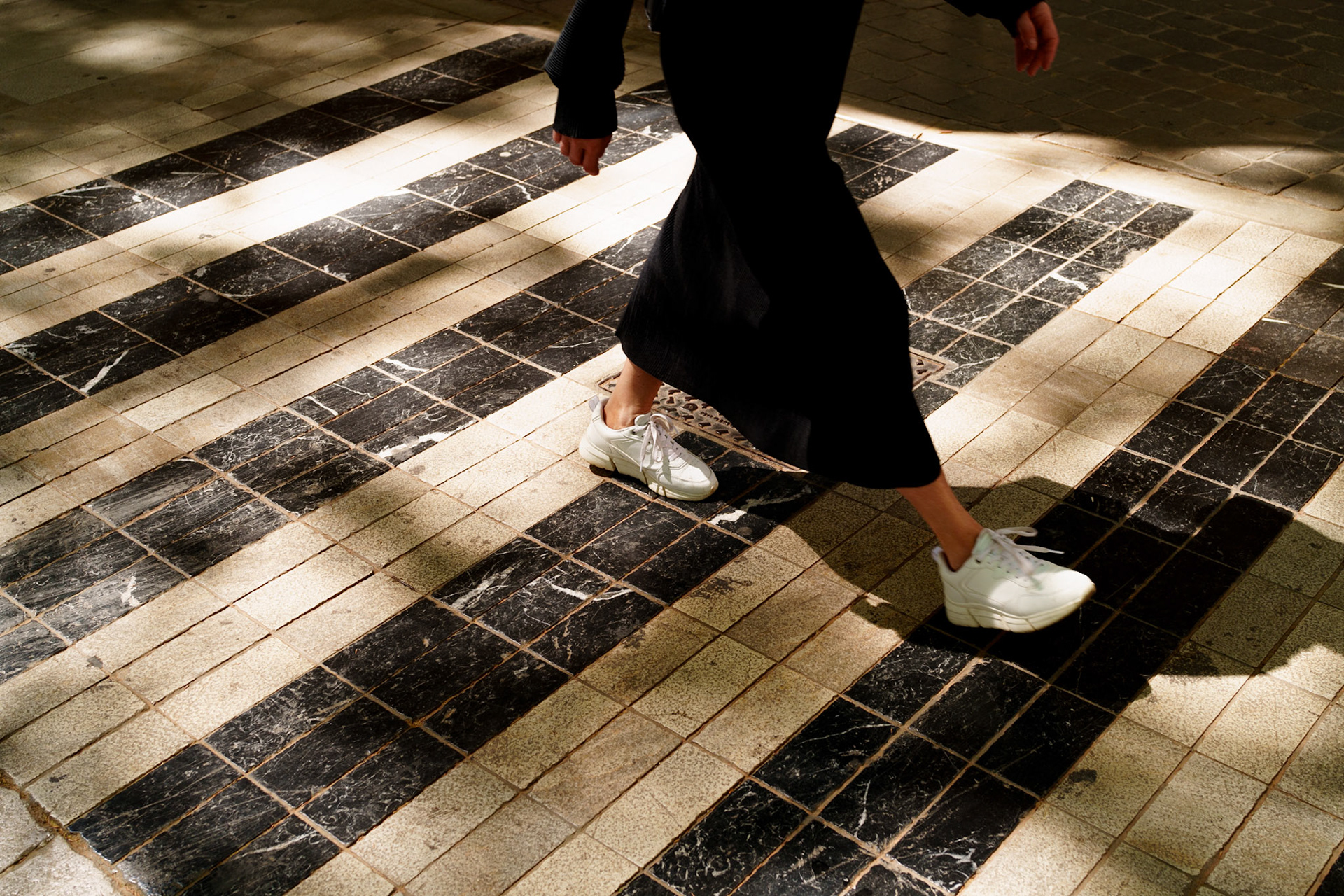 paseo borne, palma's very own champs-élysées, is awash with the rhythmic ballet of pedestrians, and here, the play of light through the foliage casts a checkerboard across the path. a snapshot captures a fleeting moment—a dance of shadow and light around the steps of a passerby. the contrast of the sunlit squares and the deep shadows, mirrored by the black and white tiles underfoot, creates a dynamic stage for the everyday promenade. it's a scene of motion and stillness, a slice of life amidst the elegance of this bustling boulevard.