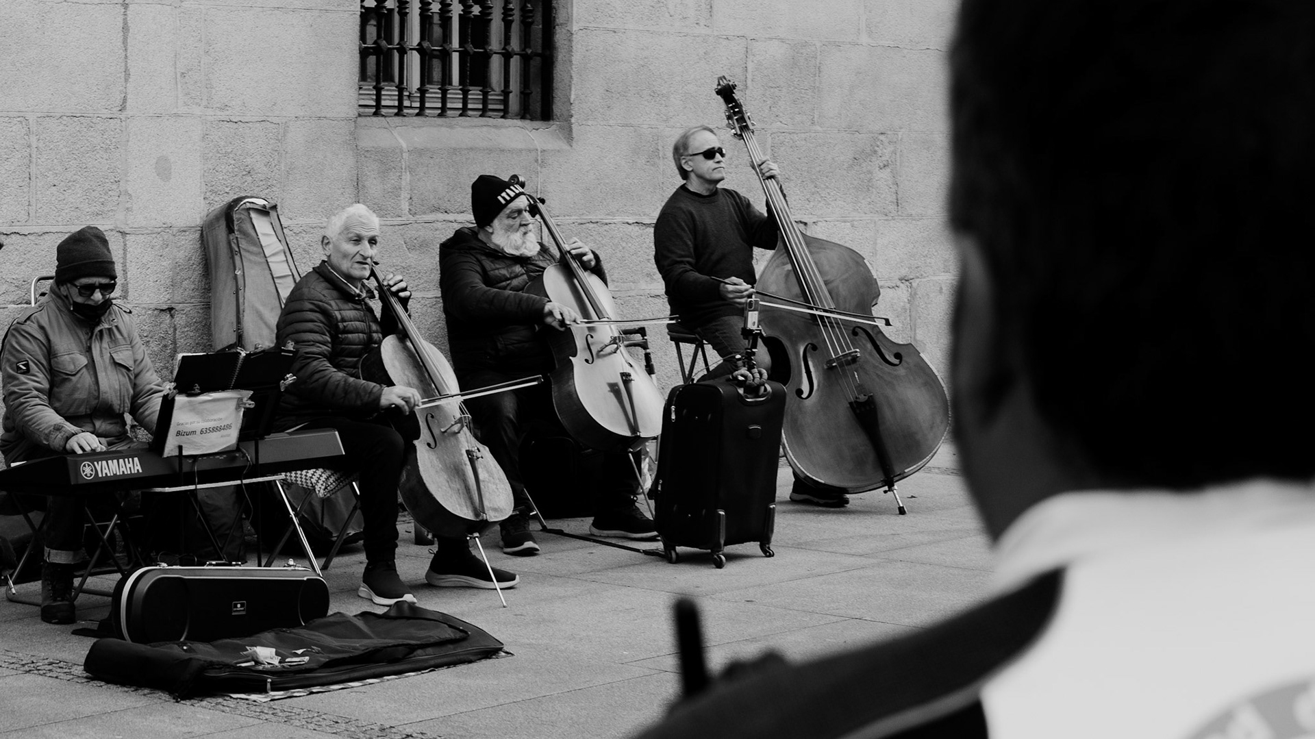 nestled between the bustling arteries of sol and gran via in madrid, an impromptu quartet breathes life into the crisp air of a city sidewalk. over the shoulder of a watchful police officer, the scene unfolds: seasoned musicians, each cradling a cello, serenade the passersby with a repertoire that whispers of bygone eras and contemporary beats. their instruments, worn yet resonant, paint aural brushstrokes against the urban tapestry. amidst the city's relentless pace, their music offers a momentary retreat—a symphony set against stone, inviting anyone within earshot to pause and savor the richness of the moment.