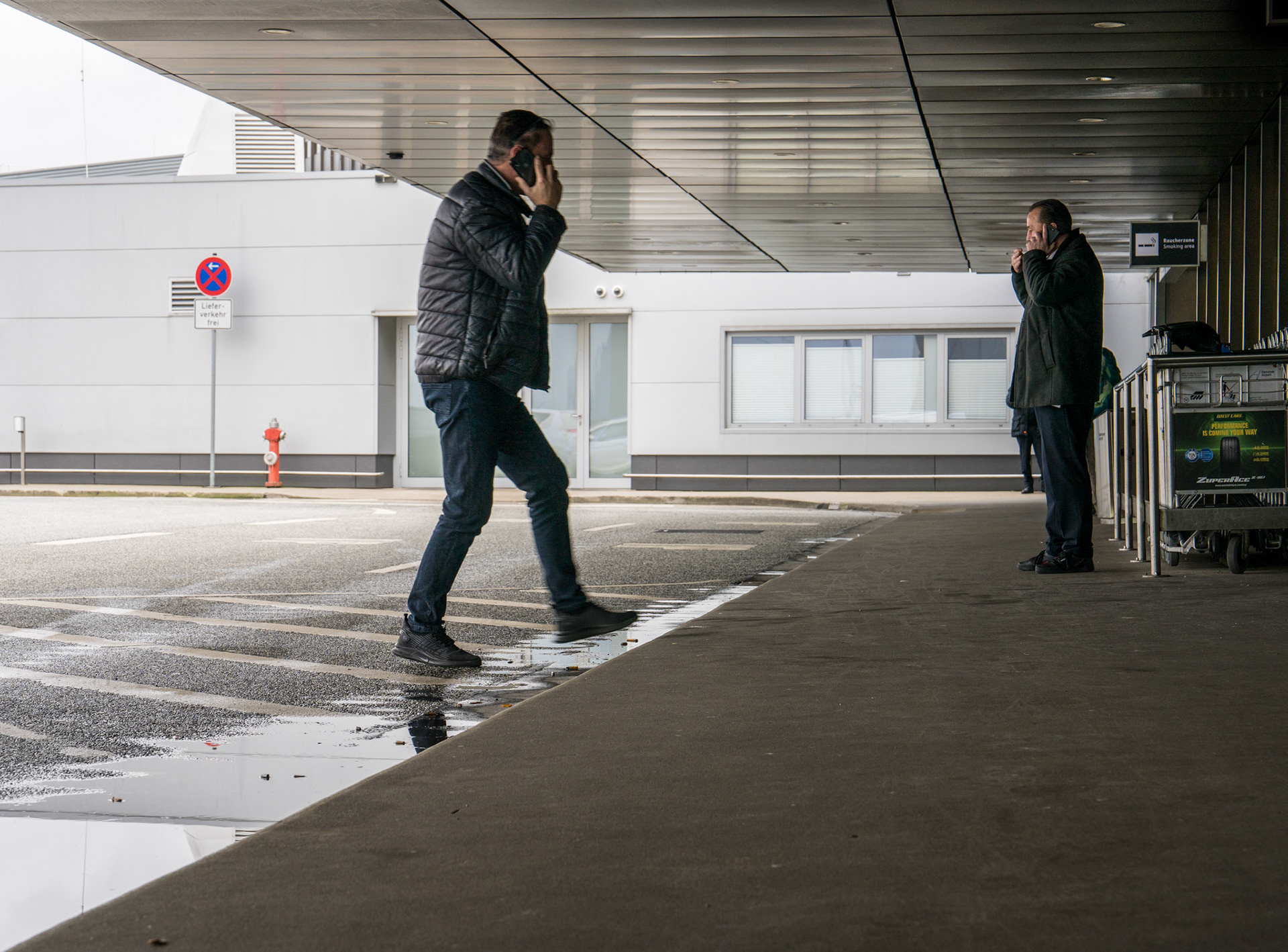 on a brisk winter day at hannover airport, life unfolds in a symphony of movement and pause. one man strides purposefully, phone pressed to his ear, caught in the swift current of travel. nearby, another stands still, savoring a cigarette, a solitary figure against the backdrop of an airport in constant motion. their parallel stories—a vivid portrayal of modern transit—reflect the contrasting rhythms of life's journey.
