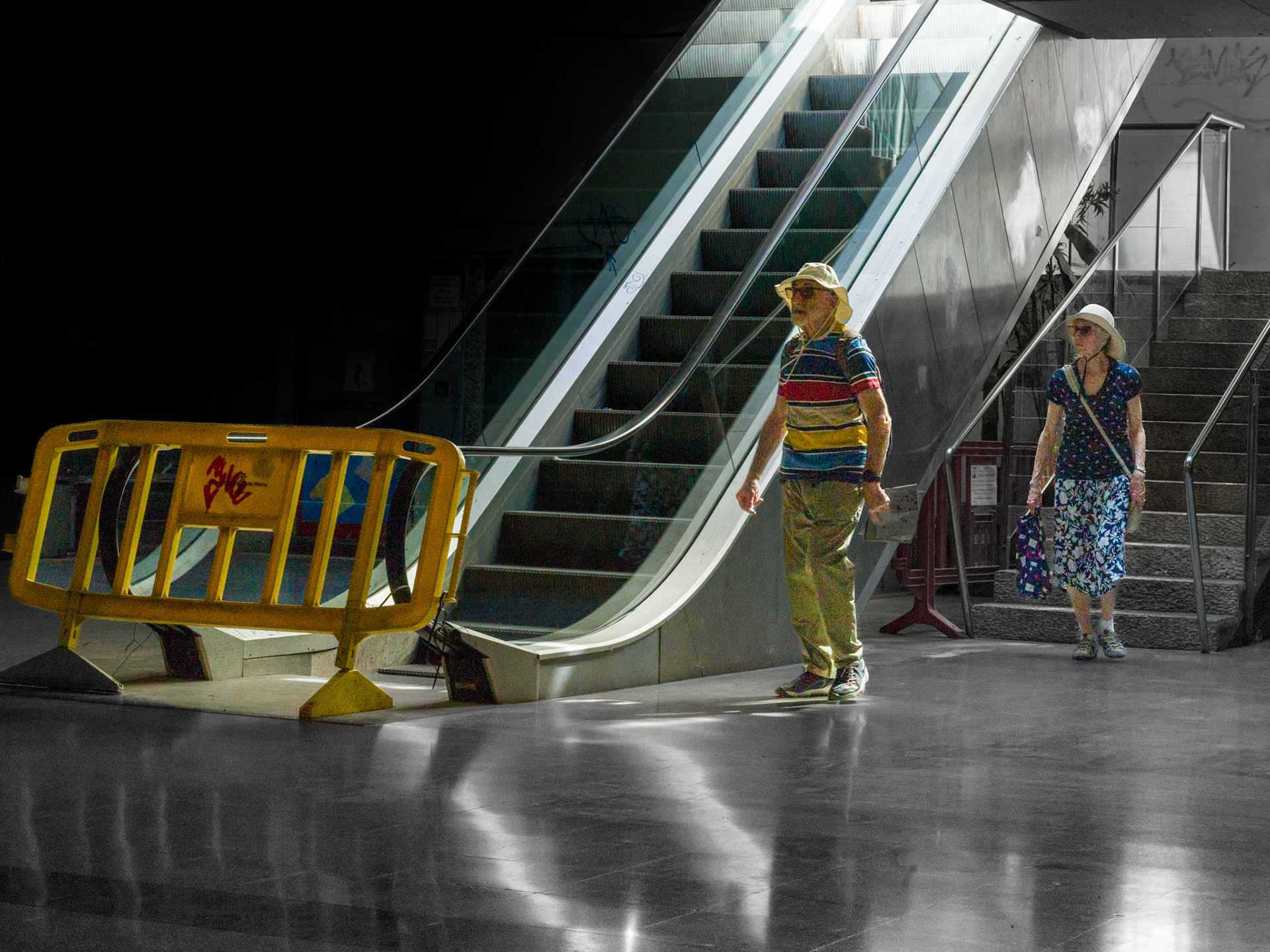 under the warm mallorcan sun, they navigated their way, but here, in the belly of palma, the tourists lost themselves in a labyrinth of escalators and shadowed corners. the bright barrier almost seems like a warning – a division between the bright world above and the quiet, hidden spaces of the city. the barrier and their summer clothing highlight them in the dark scene, as if unintentionally standing in the spotlight while the city around them tells its own quiet story.