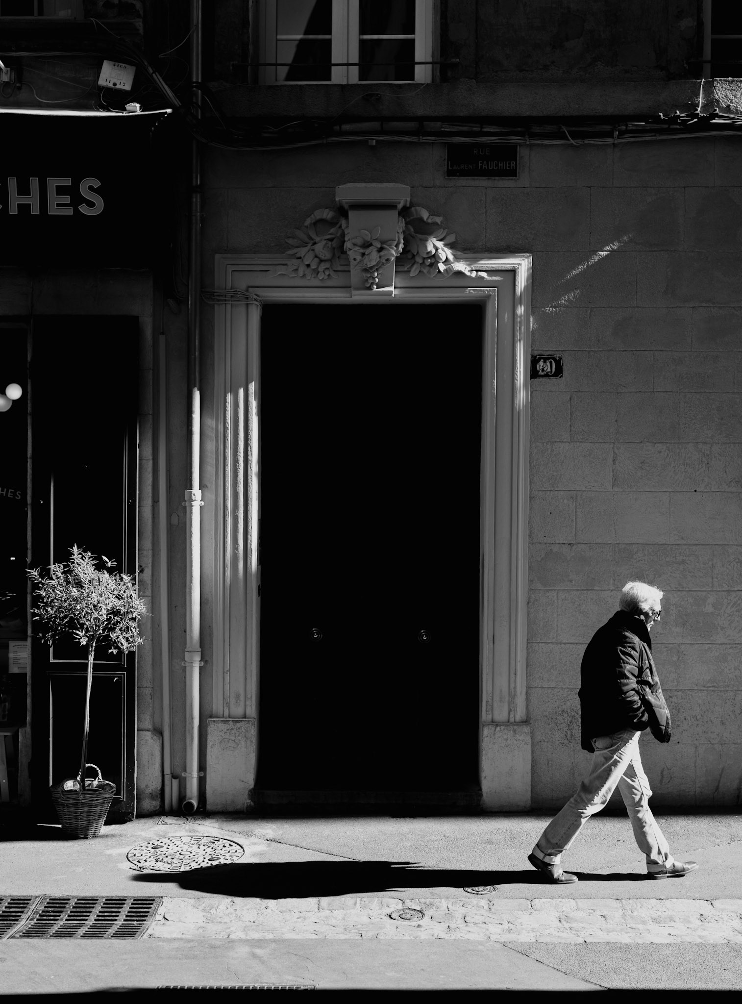 the photograph captures a fleeting slice of time on the streets of aix's old town, a study in light and life passing by. a man walks alone, his figure etched in sharp relief against the ancient stones that have stood witness to countless such passings. the sunlight dances upon the architecture, sketching stories that hang in the air just as the sign rue fauchier whispers its own. amidst this timeless ballet, the man's shadow stretches long and telling, a silent companion to his thoughts, a fluid echo on the cobbles that have known so many footsteps.