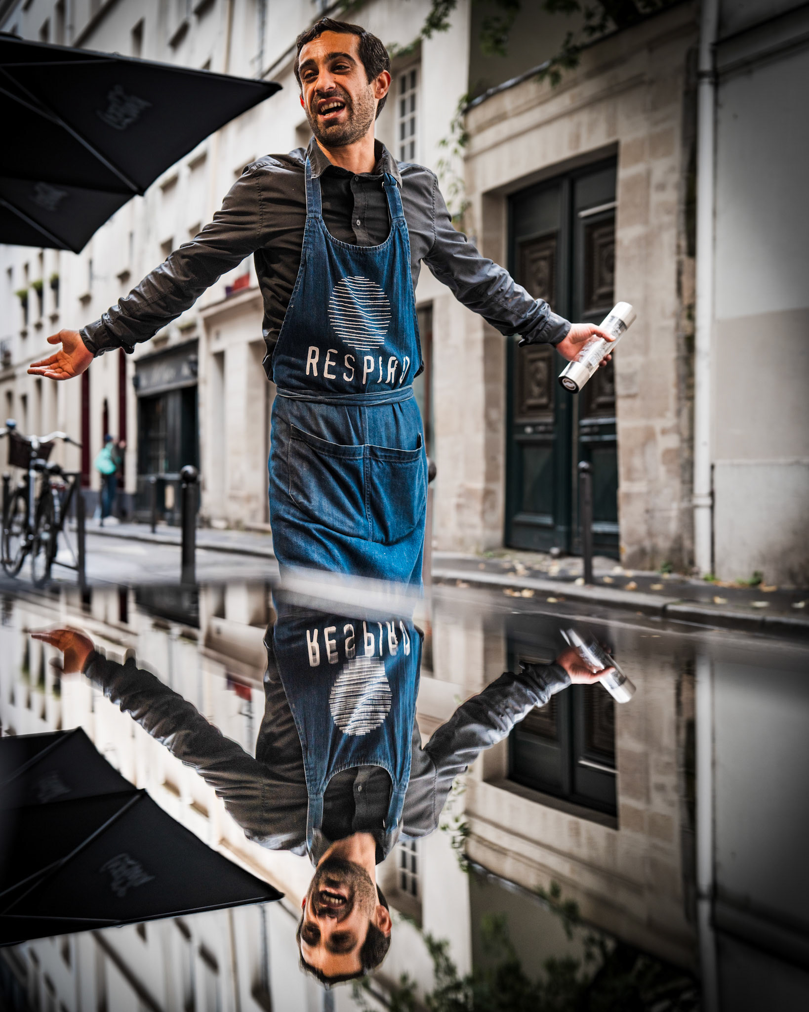 in the heart of paris, at the wonderful sicilian restaurant respiro, giuseppe served us with a smile that brightened our day, which was grey and rainy. this moment was pure serendipity, almost magical, his comedic talent, shown between serving dishes, seemed to echo through the streets. when i noticed how the table perfectly mirrored the scene, i had to capture this fleeting moment. giuseppe, completely unaware, became a living artwork in motion, caught in a step where up and down blend seamlessly. his authenticity and energy are the true soul of this photograph.