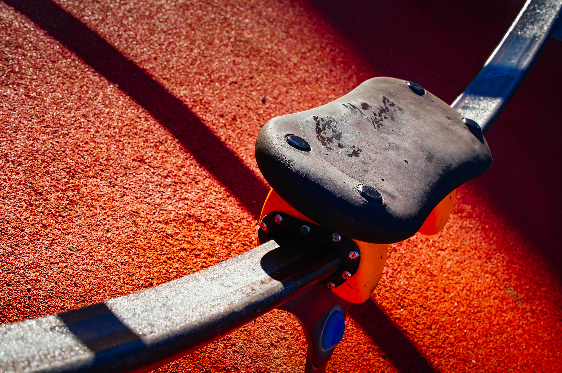 captured in palmanova, this photo is part of "a morning at the playground" series. the winter sun casts long shadows, creating a stark contrast against the vibrant red safety surface. the playground stands quiet, its colorful spring rider poised in stillness, waiting for the laughter and chaos of play that comes with the warmer days.