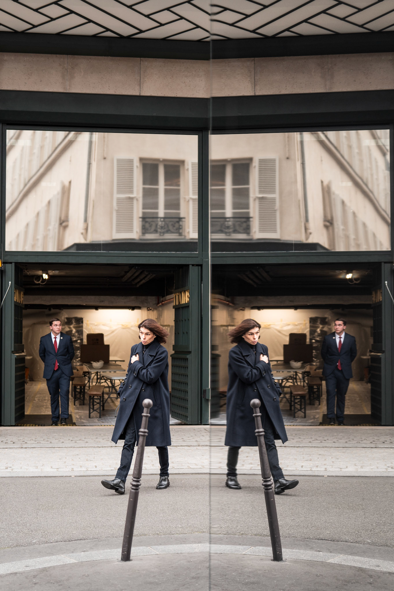 in the heart of paris, just behind the grandeur of the samaritaine, this photo captures the fleeting nature of human presence amidst the city's old-world elegance. the mirror-like reflection creates a disorienting yet poetic duplication, as if reality is momentarily fractured. a woman walks briskly, her reflection echoing her movements, creating a sense of motion even in stillness. behind her, a man in formal attire stands, observing the scene, rooted in contrast to her forward momentum. the symmetry of the frame, split by the polished glass, adds an element of surrealism, as though the everyday street has become a stage where characters from different worlds intersect, unaware of the stories they are co-creating. the muted colors and soft light evoke a sense of melancholy and timelessness, where the streets of paris whisper untold stories through their reflections.