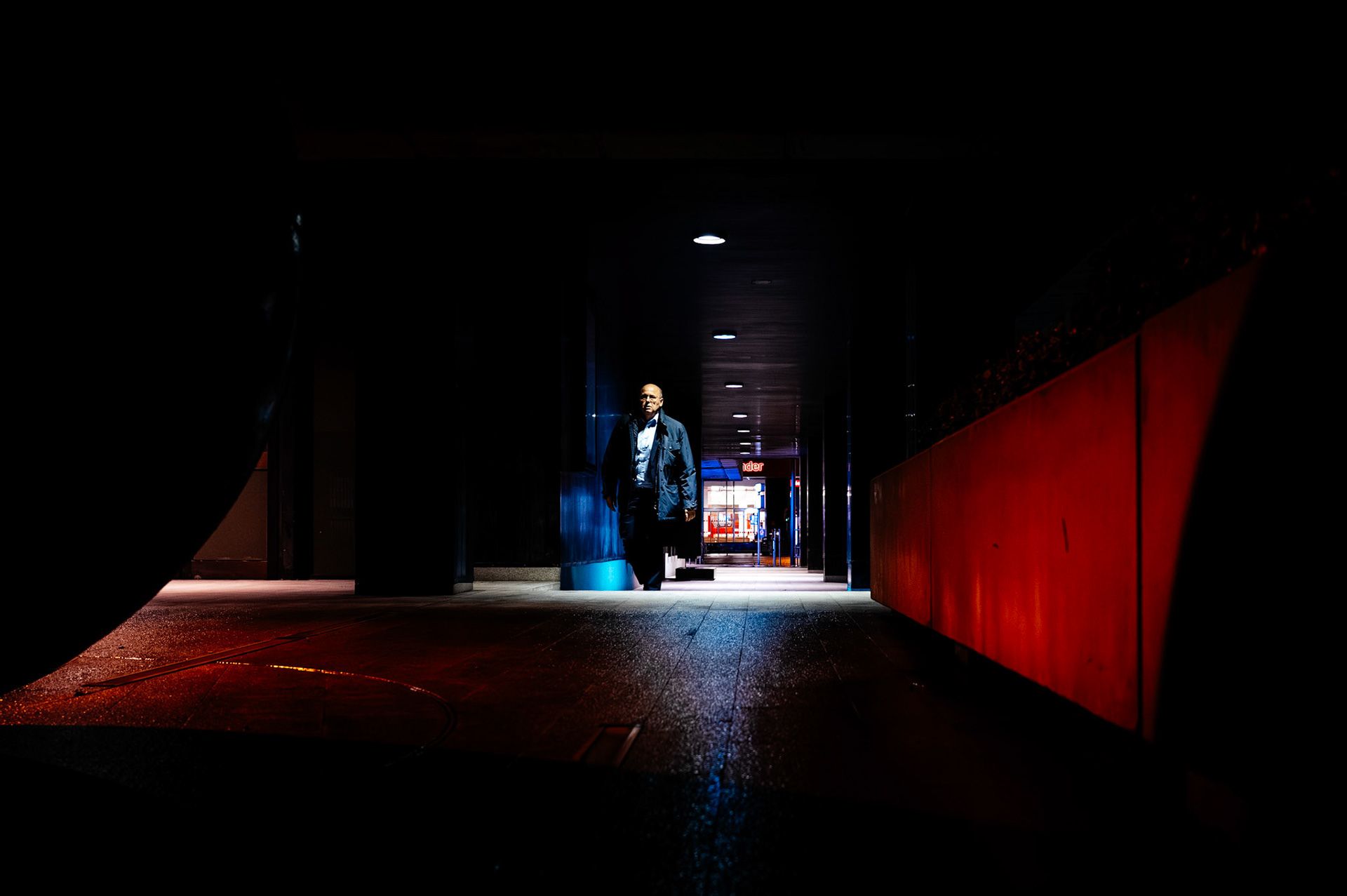 on a winter evening in the pere garau district of palma de mallorca, a lone man emerges from the shadows. bathed in the stark light of the urban landscape, he walks with purpose, his figure etched against the shop-lit corridor that leads into the heart of the city's night.