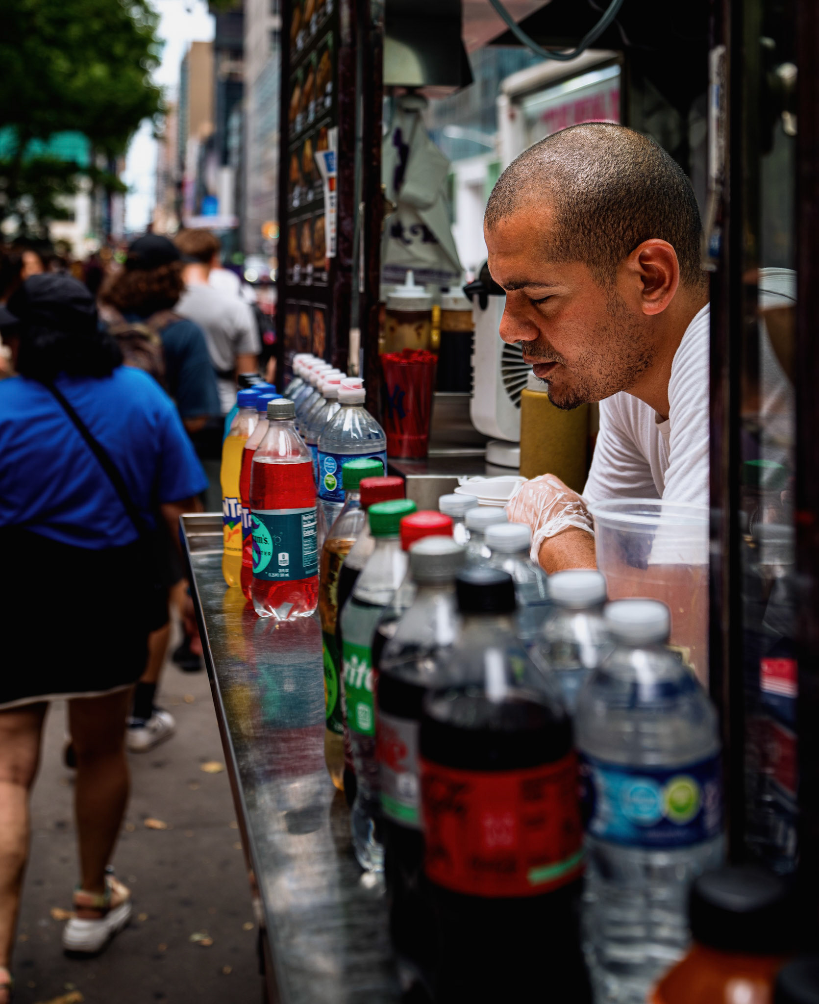 amidst the ceaseless flow of new york city's streets, a vendor takes a moment to rest, his expression reflecting the weight of the day's labor. the vibrant colors of bottled drinks contrast with his tired demeanor, illustrating the dichotomy of the city's hustle and the personal toll it takes. this image captures the essence of urban resilience, where each individual navigates their own journey within the larger, relentless rhythm of city life.