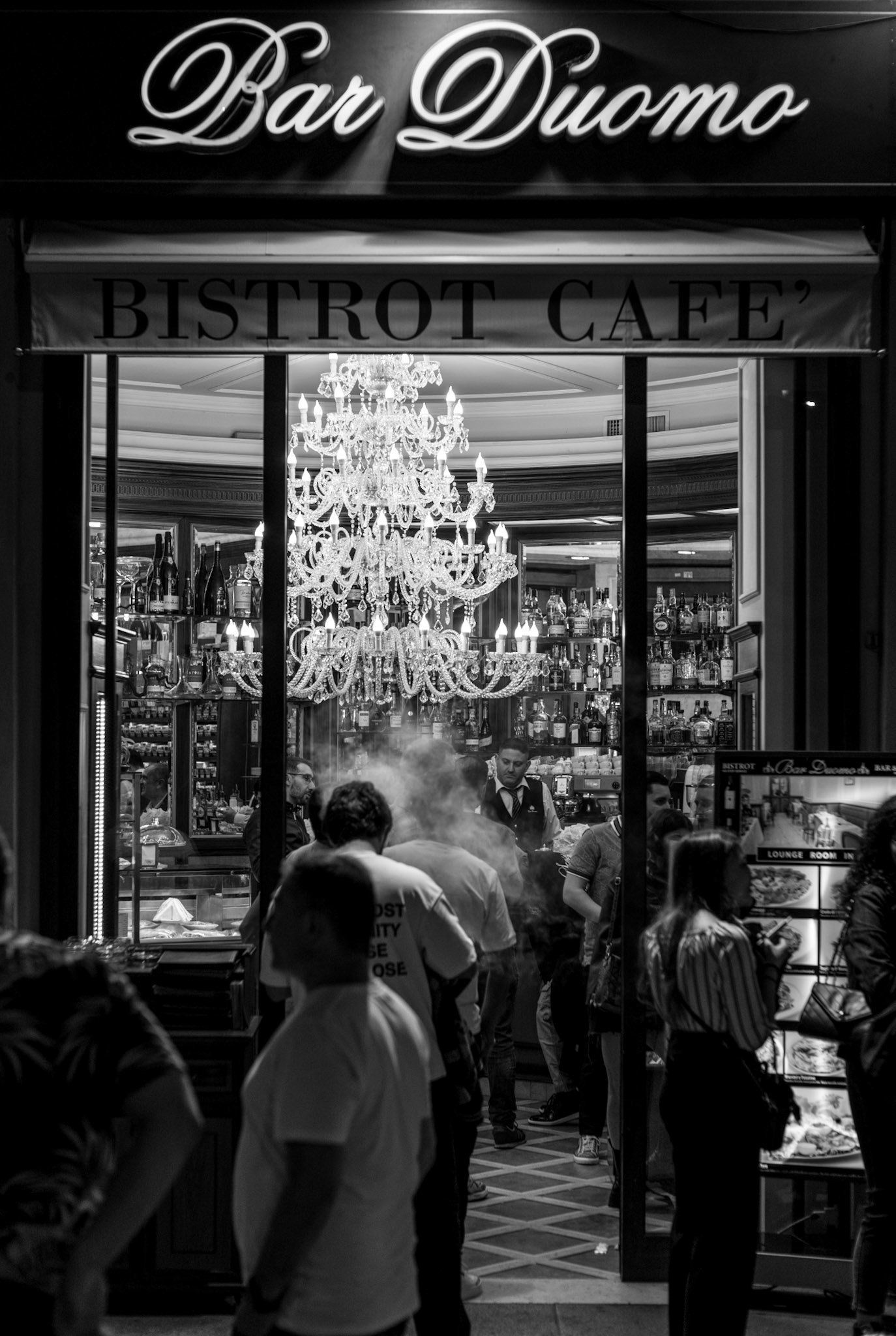 just steps away from the grandeur of milan's cathedral, bar duomo stands as a beacon of the evening's warmth. a chandelier inside spills crystals of light, mingling with the hum of the night's patrons. here, amidst a haze of conversation and the ballet of waitstaff, milan's pulse is felt. it's a vignette of urban melody, where history casts a long shadow and every coffee is a subtle ode to the city's heartbeat.