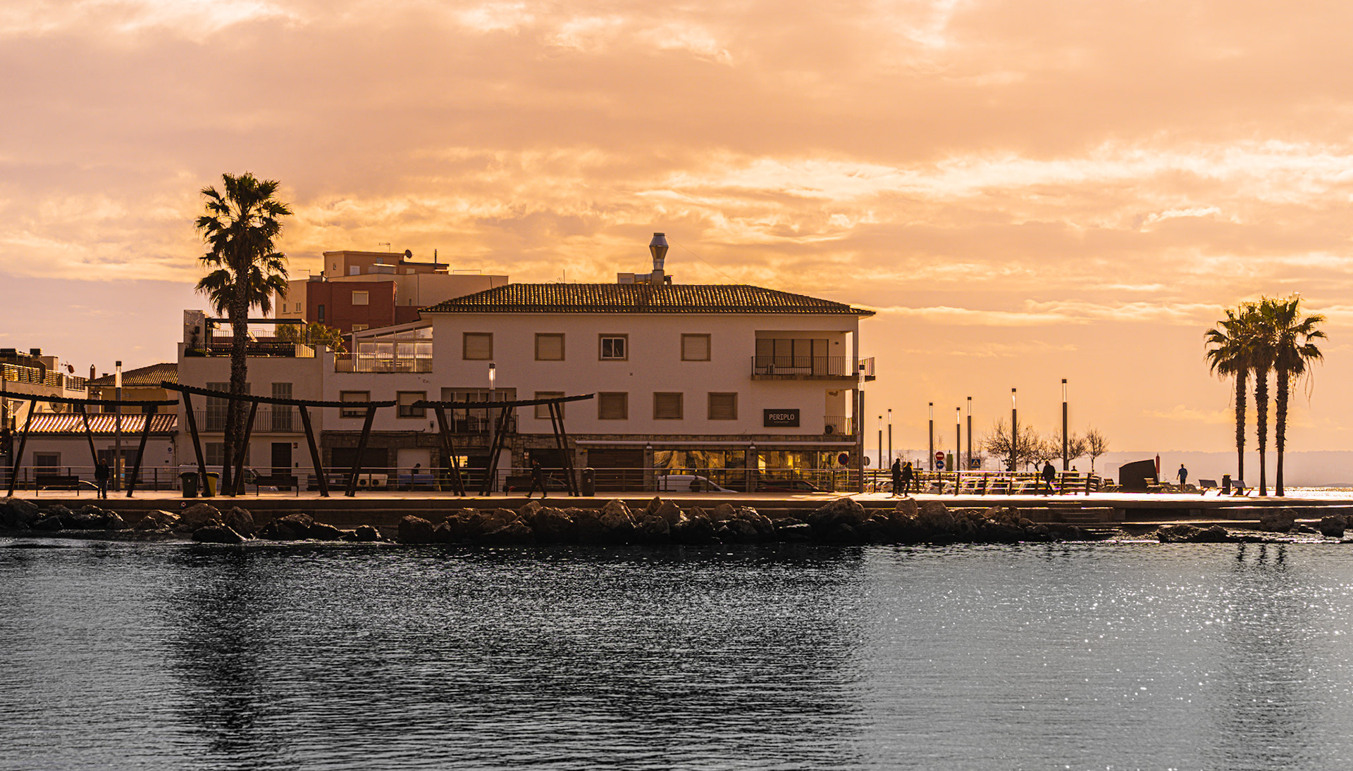 in the bay of portixol, the sun casts a golden glow over the tranquil waters. facing the renowned restaurant periplo, the scene is a peaceful morning tableau. locals and visitors alike frequent this beloved seaside district of palma, where the mediterranean lifestyle is embodied in leisurely mornings and scenic waterfront views.