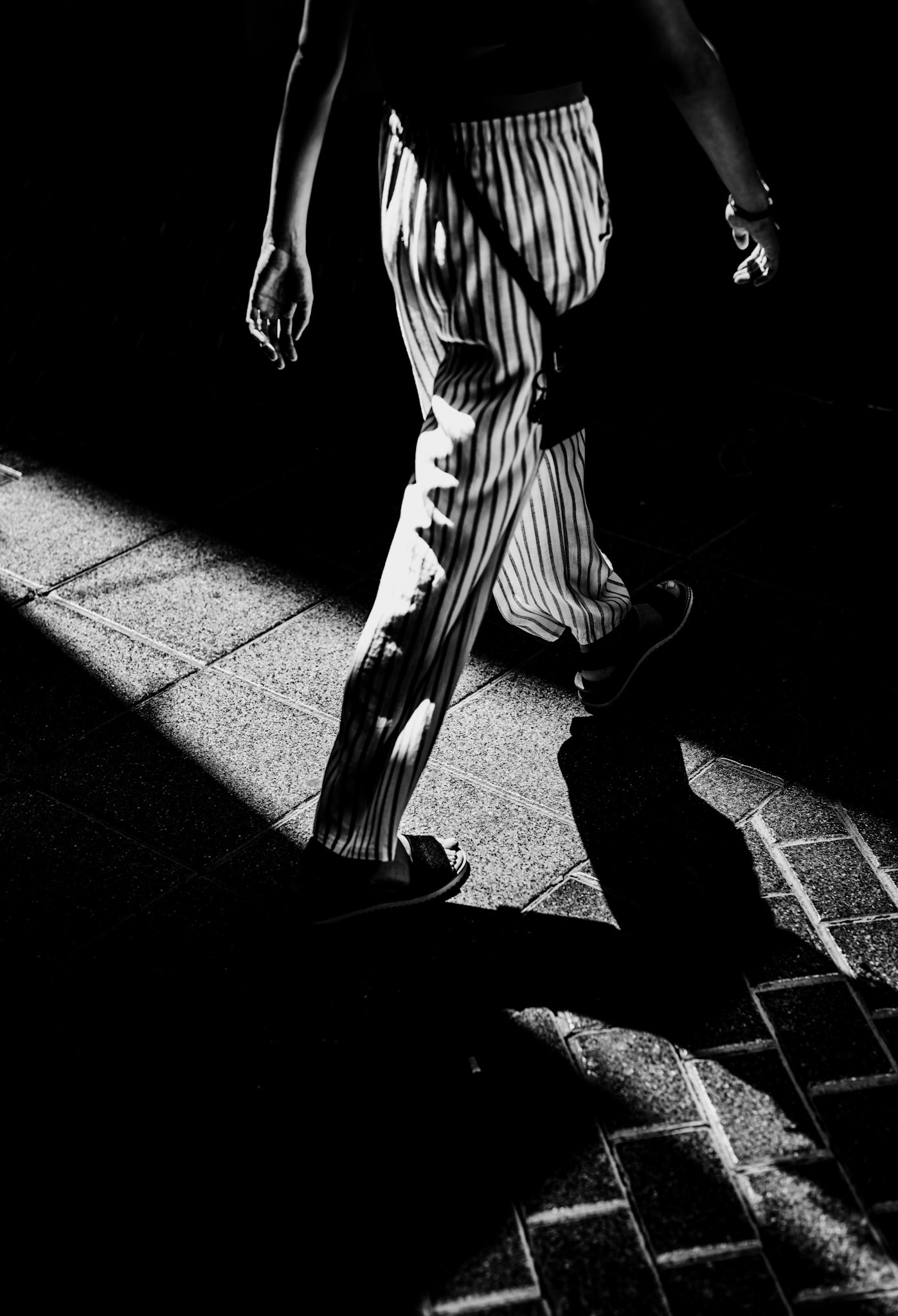 in the narrow, winding streets of palma de mallorca's old town, i captured this fleeting moment of a figure walking through the dance of light and shadow. the sharp contrast between the sunlight and the shadow creates an almost abstract composition, with the striped pants adding a rhythmic element to the scene. the anonymity of the subject and the focus on the lower half of the body invite viewers to imagine their own stories about this urban wanderer. the old town's historic ambiance enhances the timeless quality of the photograph, making it a poetic tribute to everyday moments often overlooked.