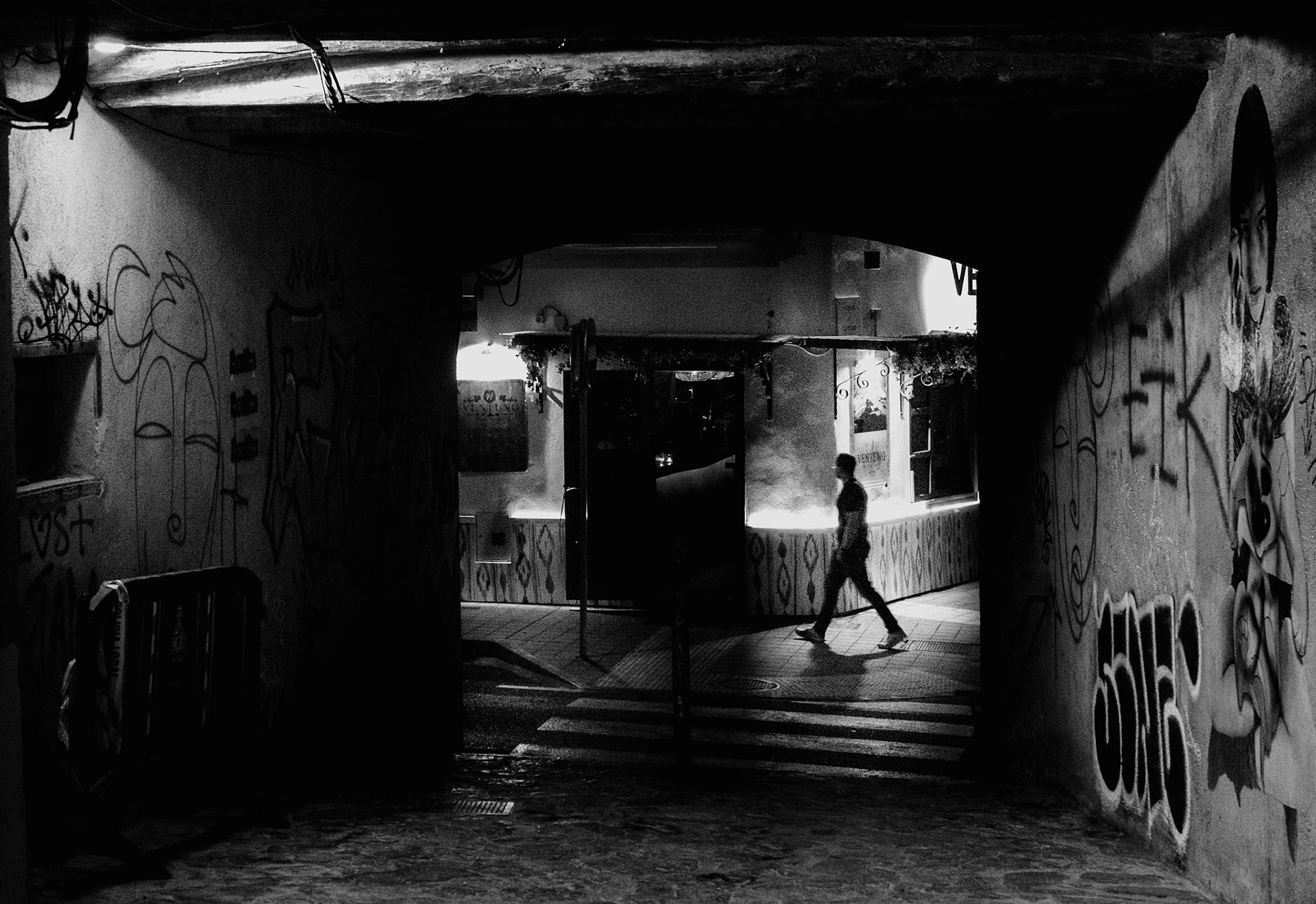 in the heart of santa catalina, a district known for its pulsating energy in palma de mallorca, the night whispers stories on its walls. here, under the cloak of darkness, a solitary figure traverses the graffiti-laden alley, his silhouette a fleeting ghost against the chiaroscuro of streetlights and shadows. this monochromatic scene captures the essence of the night—a fusion of art, mystery, and the quiet drama of urban exploration.