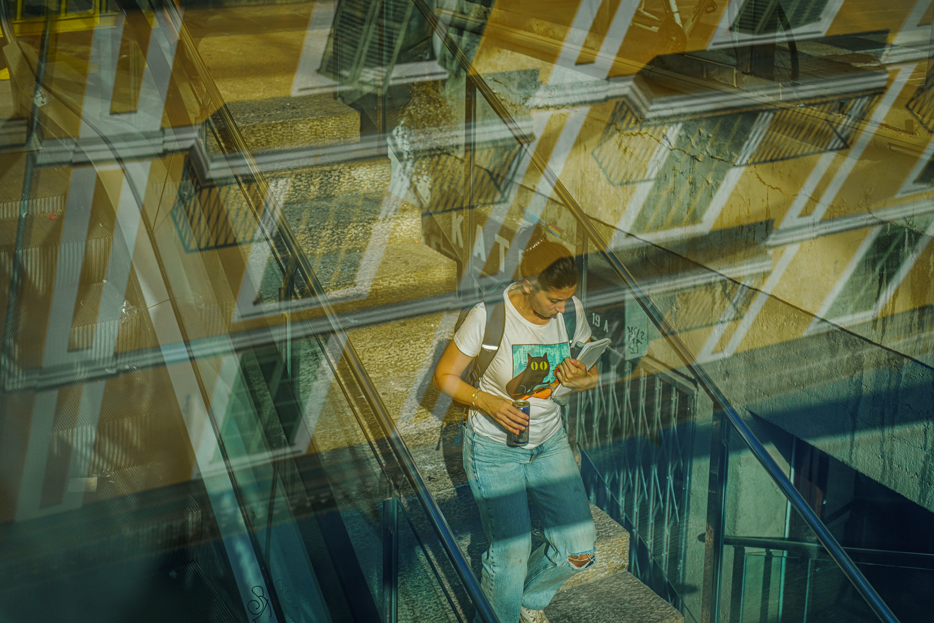 beneath the bustling plaça mayor in palma, this stairway leads down into a quiet space—a once lively shopping center, now a hollow memory filled with echoes of its past. the bright yellow façade reflects the architectural charm of the plaça mayor above, but down here, the scene tells a different story. the empty storefronts and forgotten corridors contrast sharply with the vibrant street life above. reflections of buildings overlay the image, blurring the lines between the old and the new, the lively and the abandoned, the present and the past. a subtle reminder of how time can change spaces, leaving behind only the silent witnesses of what once was.