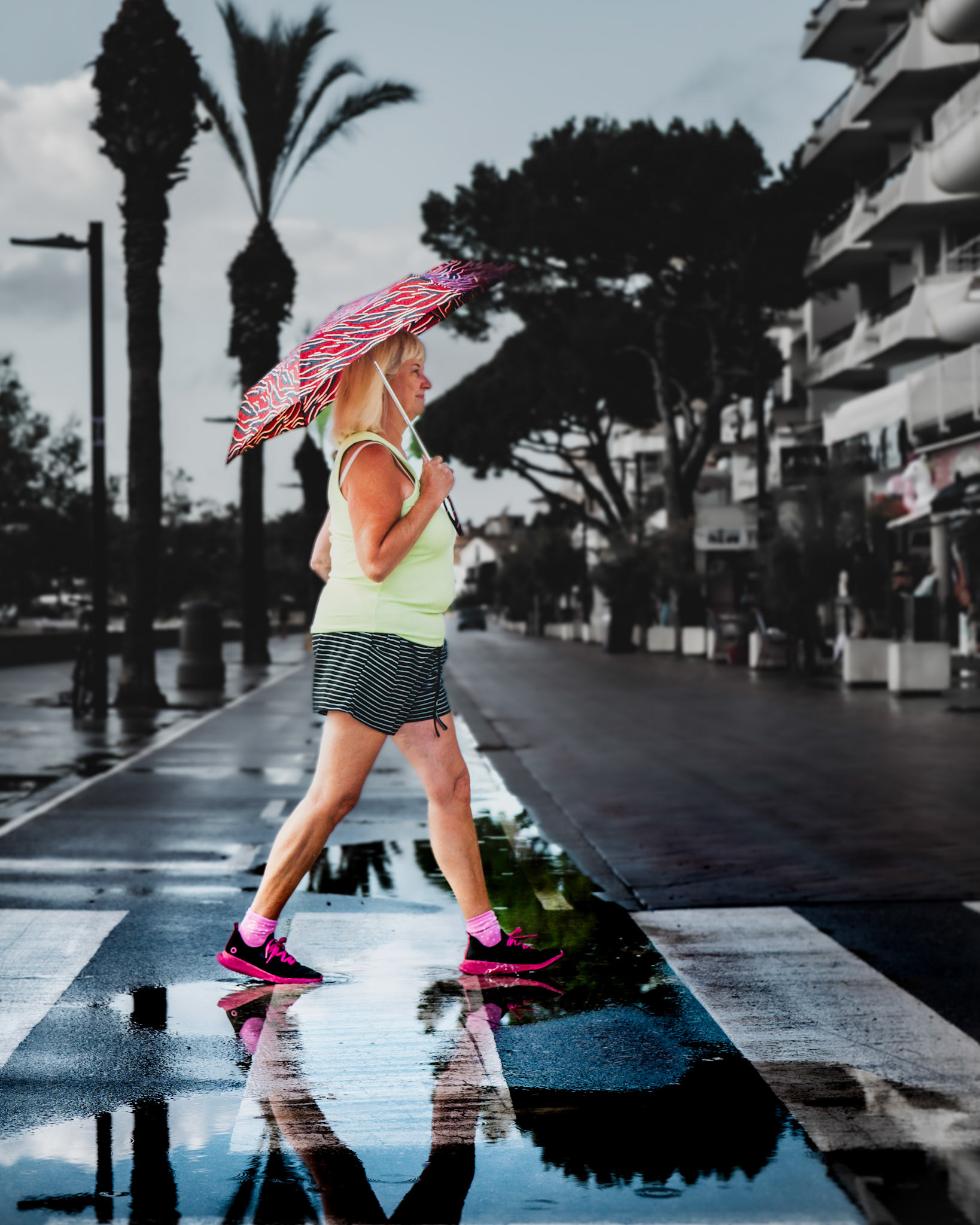 captured on a quiet, rainy morning in Port de Pollença, the streets were still wet, reflecting the palm trees and the determined steps of a lone walker. her bright pink shoes and colorful umbrella add a splash of energy to the otherwise subdued scene. she walks with purpose, her reflection trailing behind her in the puddles, as if the rain has invigorated her. the calm after the storm made for a beautifully serene and spontaneous moment.
