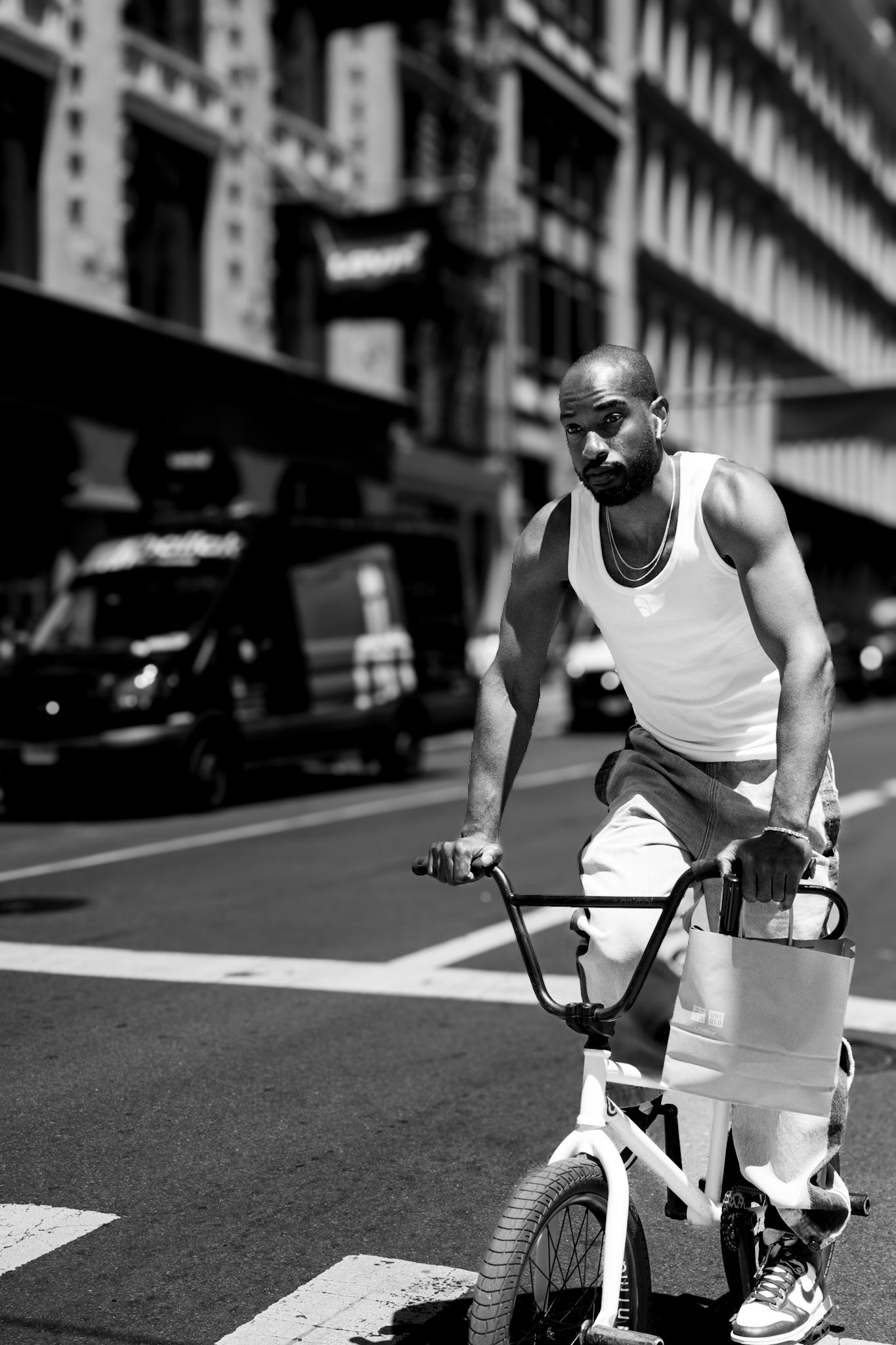 the streets pulse with energy, but this moment belongs to him—focused, steady, cutting through the noise of the city. the sun catches his shoulders, casting shadows that accentuate his strength and determination. his hands grip the handlebars firmly as if controlling not just the bike, but the rhythm of the street itself. the blurred buildings and vehicles in the background form a contrast to his sharp, unwavering presence. it's a snapshot of movement, where the city's chaos becomes a stage for a quiet, personal journey.