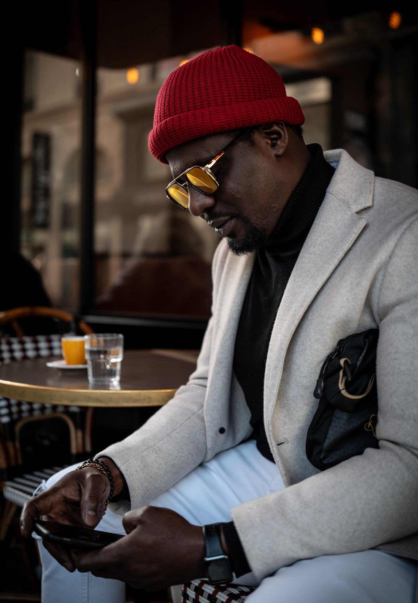 in the heart of paris, nestled at place d’estienne d’orves with a view of the majestic eglise de la sainte trinité, a man sits quietly at café du mogador. the soft light gently frames him, bringing out the contrast between his vibrant red beanie and the calm café ambiance. absorbed in his thoughts, with a glass of water and orange juice at the ready, his world feels distant from the bustling parisian streets. the scene captures a peaceful, intimate moment of pause in the city of lights, against the backdrop of historical beauty.