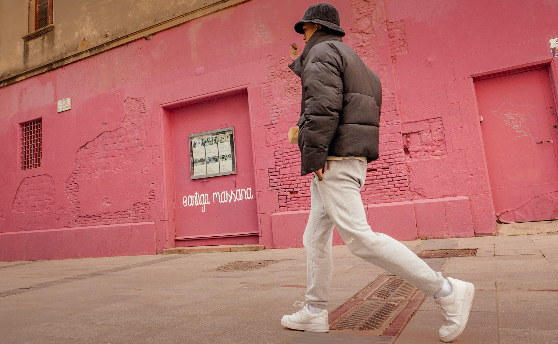 n the old town of barcelona, a passerby strides along a striking pink backdrop, a vibrant contrast to the muted tones of their attire. the walls whisper tales of the past, with patches and textures speaking to the city's rich tapestry. it's a scene where urban life and colorful history intersect, with each step along the cobbled streets adding to the narrative of this bustling catalan corner.
