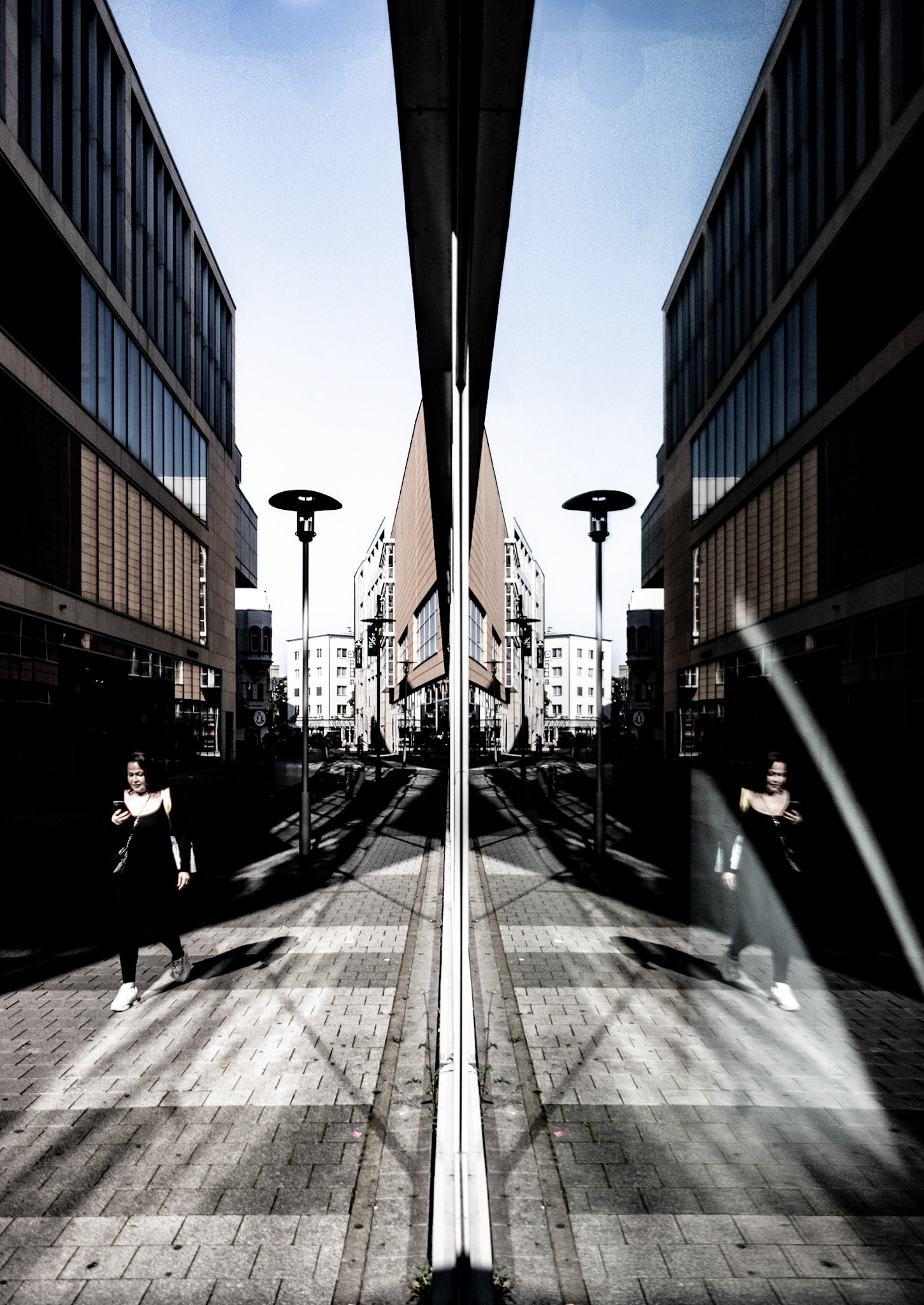 in the heart of downtown hannover, where everyday life pulses past glass facades, i captured this fleeting moment. the reflection both divides and unites reality, like a portal into a parallel version of the city. the solitary figure, engrossed in her smartphone, symbolizes modern isolation amid the urban landscape. the leading lines pull the viewer's gaze deep into the scene, while the light dramatically highlights the architecture and the woman. it’s a quiet, surreal moment that reveals the contrasts of urban existence.
