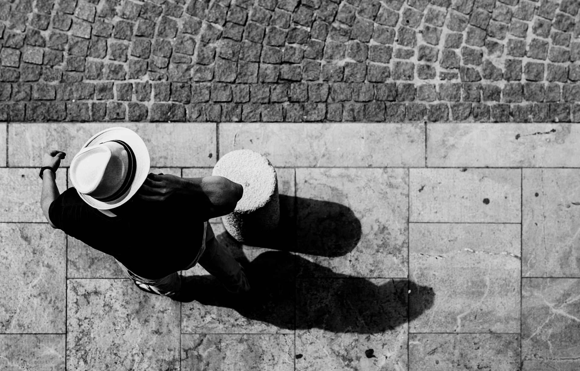the elegance of a hat, the shadows cast on the stone pavement, and the classic street photography motif come together in this scene. captured from the balcony of a charming apartment, this photograph showcases a tourist in saint-tropez, aligned with the timeless appeal of street photography, blending seamlessly with the historic ambiance of the old port.