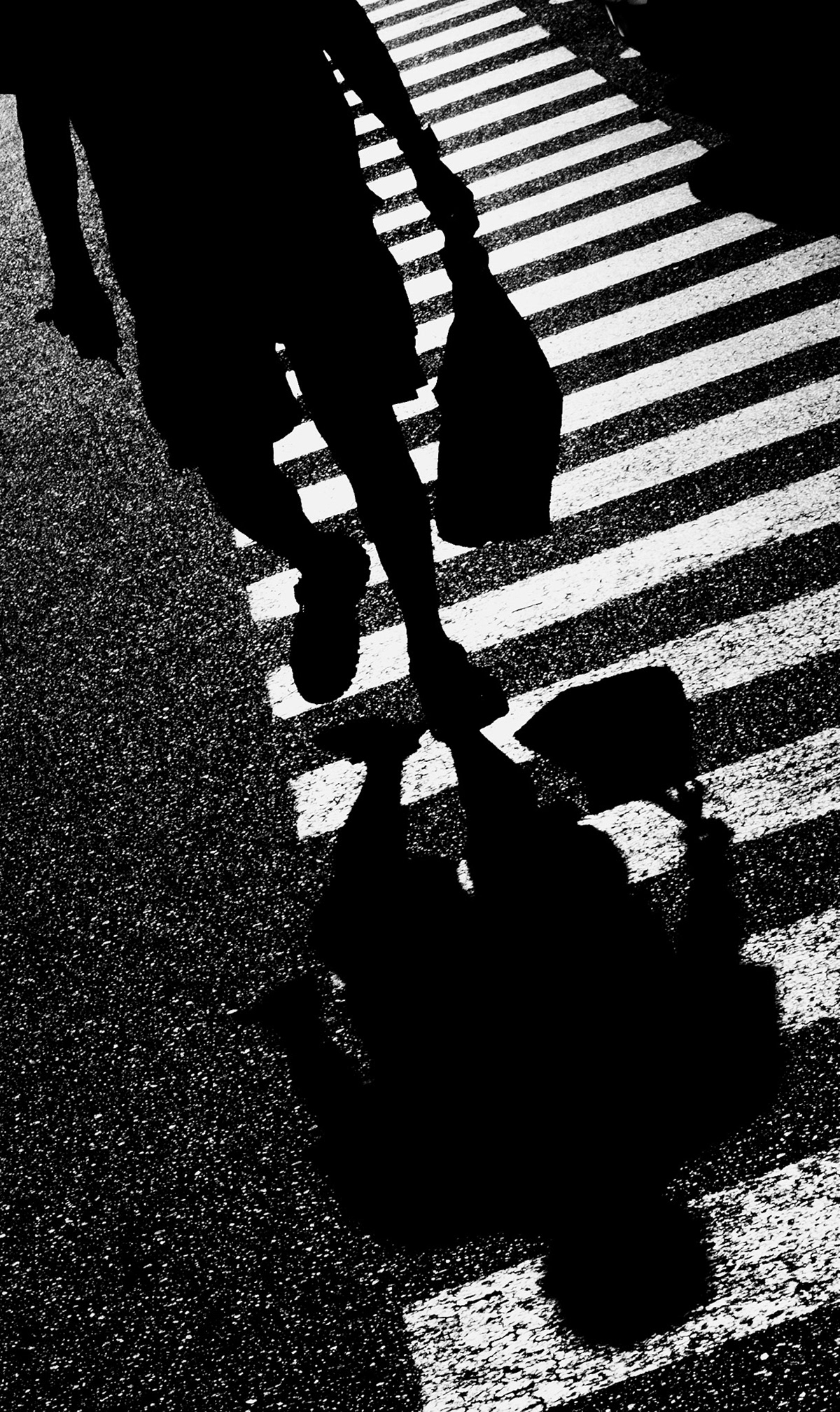 in the bustling parking lot of the mercadona supermarket in palmanova, a solitary figure crosses the zebra stripes, casting a stark silhouette against the glistening pavement. the harsh light of the mediterranean sun creates a dramatic interplay of shadows and highlights, turning the mundane act of crossing a street into a moment of abstract art. the figure’s shadow stretches and distorts, echoing the fleeting nature of our daily journeys. this image captures a transient moment, where light and dark dance together in an urban ballet, reminding us of the beauty hidden in everyday scenes.