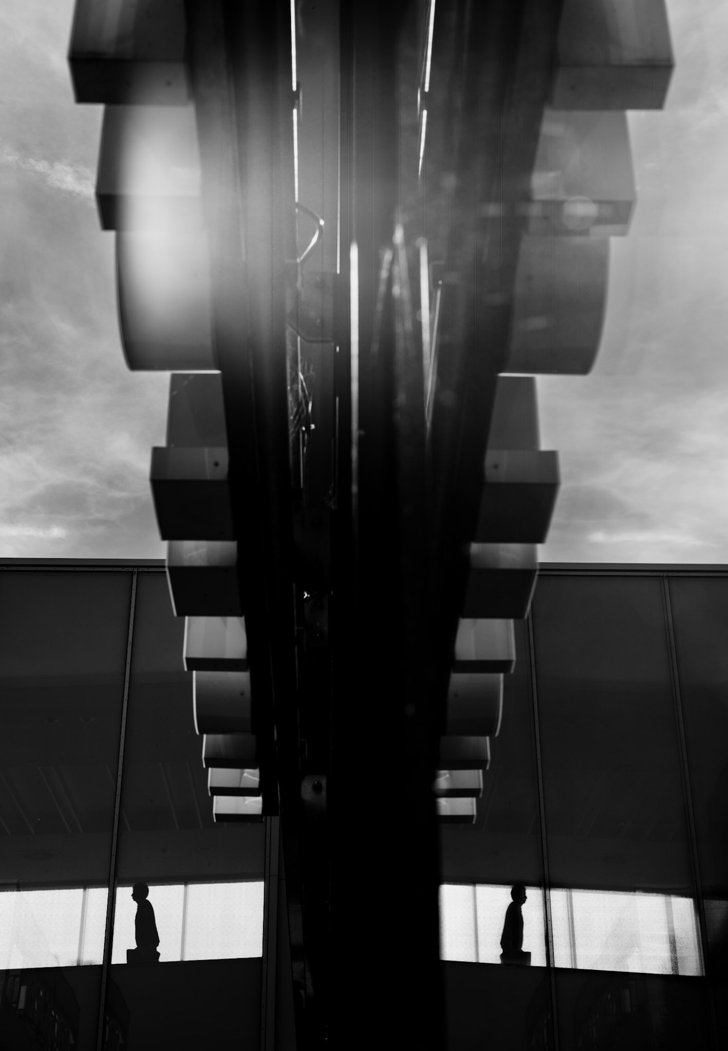 in the polished glass of the riem arcaden, reality blurs and doubles. a lone silhouette walks along the bottom edge, faint but purposeful, a shadow that seems both part of the structure and somehow detached from it. overhead, strong industrial shapes reflect and intersect, softened by a faint light that filters through and dissolves the lines into a hazy abstraction. this image captures a moment suspended in liminality—where reflections hold stories and the city’s architecture feels like a portal to somewhere else.