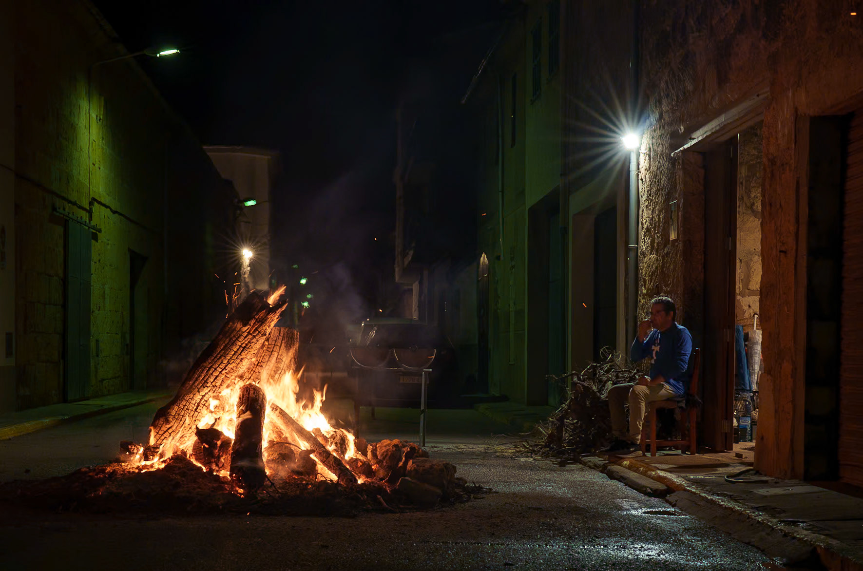 in the hushed alleyways of sa pobla, the night of san antoni whispers stories of old through crackling timbers and glowing embers. a local sits, contemplative, bathed in the warmth of tradition that cuts through the nocturnal chill. it's a scene where the modern world pauses, and a timeless ritual unfolds, kindling not just fires but a community's spirit. this festivity, steeped in the heritage of mallorca, sees the town's heart beat to the drum of unity, flickering flames dancing to the rhythm of shared tales and laughter.