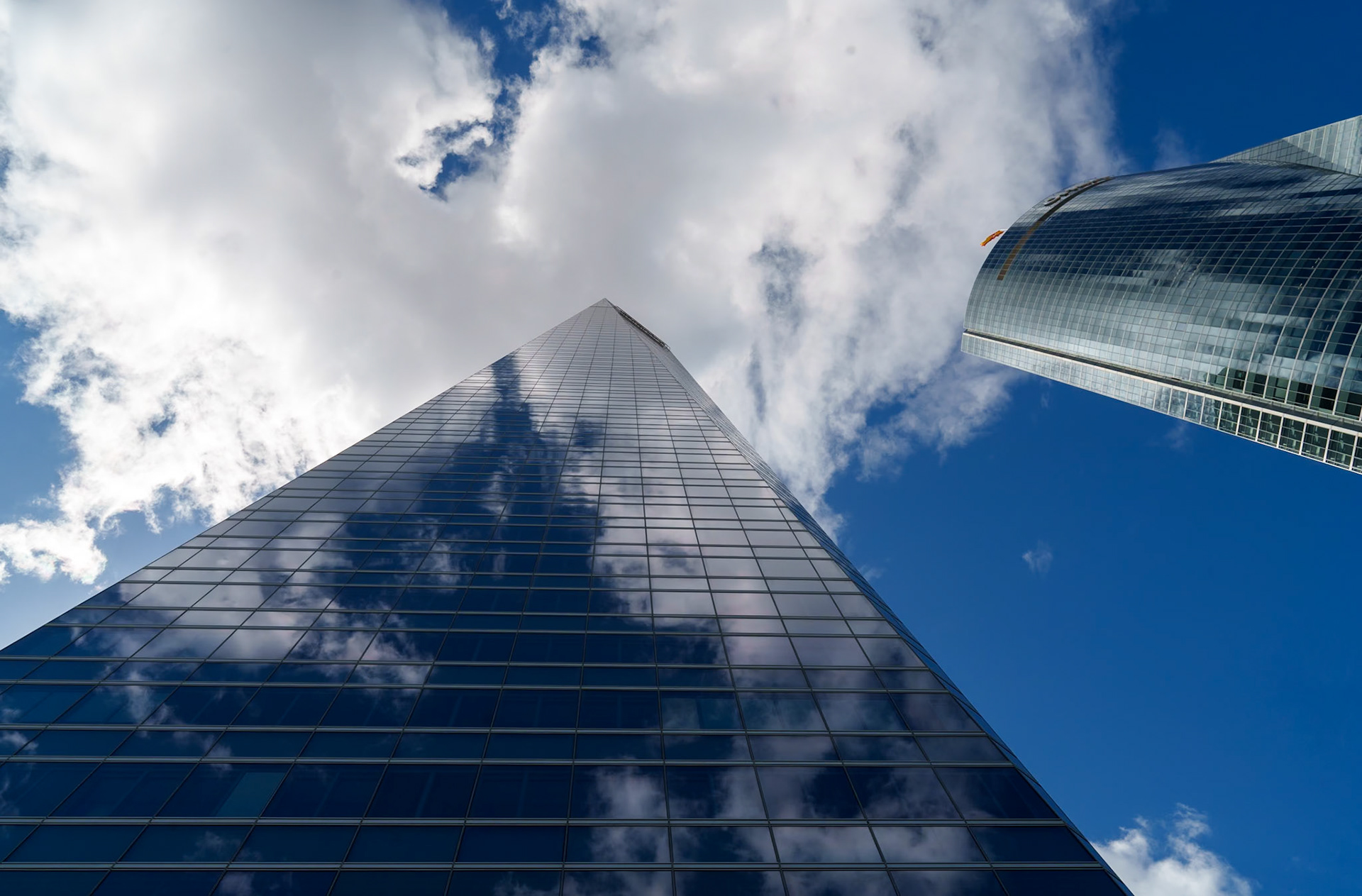 in madrid, where the "cuatro torres" stretch, two giants reach for the sky, nearly piercing the cotton-like clouds above. glass surfaces mirror the ambition of a city, reflecting fragments of blue and white in a spectacle of modernity. there's a conversation between earth and heaven here, a visual poetry of aspiration, where human ingenuity meets the artistry of the skies. the towers, like beacons of progress, stand as sentinels at the threshold of the clouds, their tips disappearing into a dreamscape where the boundaries of reality seem to blur into the ether.