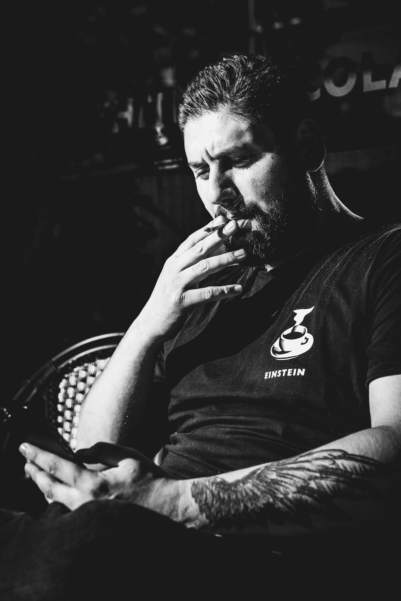 captured in front of the café einstein on berlin’s kurfürstendamm, this portrait isolates a quiet moment of reflection amidst the city's buzz. the soft cigarette smoke blends into the heavy shadows, while the light etches out the subject's deep thought and subtle weariness. a story told in gestures and expression, where the iconic café logo on his shirt hints at more than just a brand—perhaps a state of mind.
