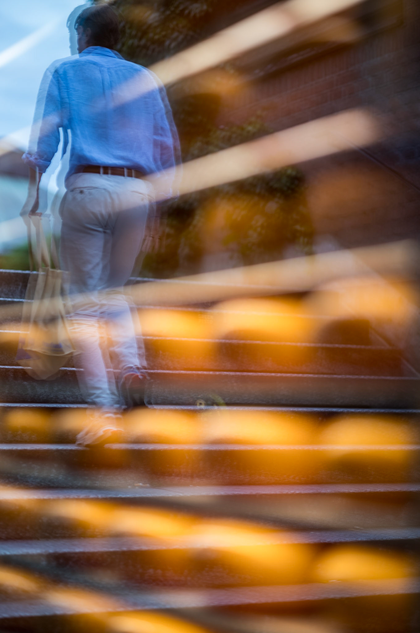 captured at a cheese shop in viktualienmarkt, this photograph beautifully juxtaposes the rush of modern life with the timeless allure of artisanal goods. a man hurries up a staircase, his reflection merging with the display of golden cheese wheels in the shop window. his obliviousness to the charming scene underscores the contrast between the fleeting nature of our daily routines and the enduring beauty that often goes unnoticed.