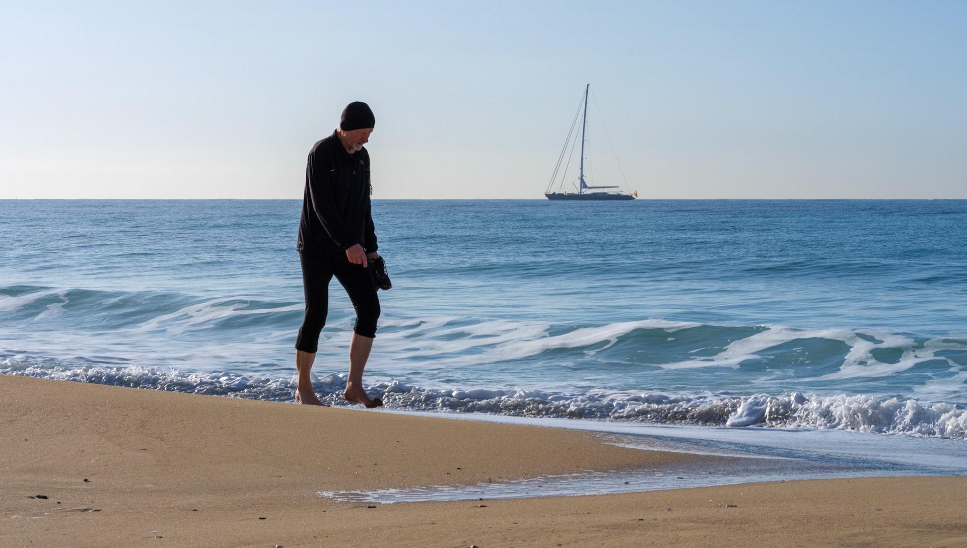 on the shore of palma's winter embrace, the beach becomes a quiet stage for contemplation. a lone observer stands, toes grazing the water's edge, as if in silent conversation with the sea. beyond, a solitary sailboat is etched against the horizon, a silent companion in the vast expanse. the air holds the chill of the season, yet the sun still whispers of the warmth to come. it's a moment caught between the calm solitude of winter and the promise of bustling summers, a breath held in the cycle of seasons.