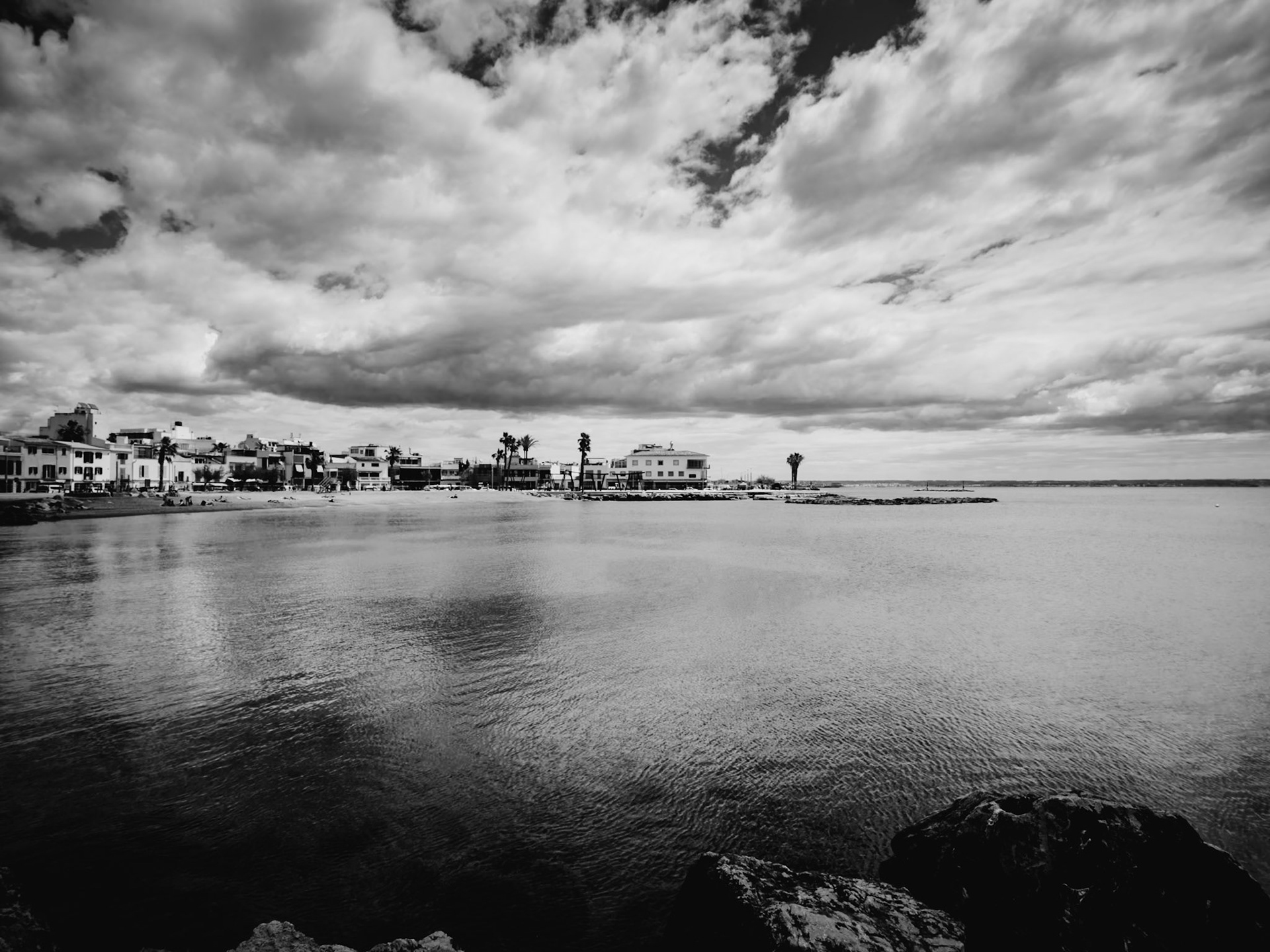 in this monochrome vision, the bay of portixol under a brooding sky presents a scene both timeless and tranquil. the grayscale tones enhance the peaceful yet somber mood, with clouds hanging low as if to whisper secrets to the calm waters below. the quiet town stretches along the waterfront, its architecture a silent testament to its serene coastal life. this photograph captures not just a location but a mood; a reflective pause where the bustling sounds of daily life seem muted by the gentle hush of an overcast day. it's a perfect blend of nature's drama and the quietude of a small town, inviting the viewer to listen to the soft echoes of portixol.