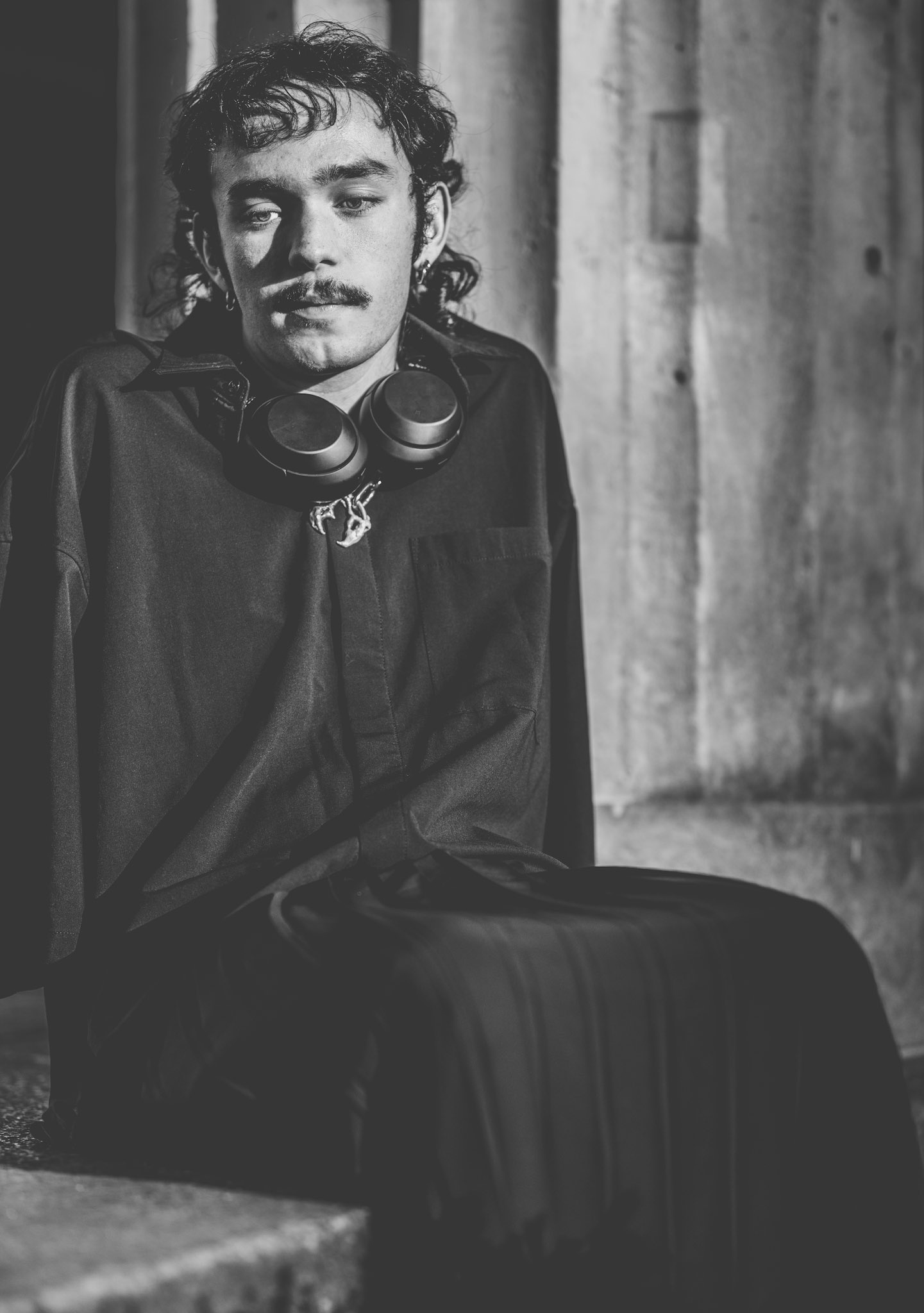 through the columns of the city, where voices fade and thoughts linger, he sits. headphones draped around his neck, yet no music plays — it’s the pause between the beats that resonate. the light catches his face, but it’s the shadow that tells the story. i asked for a photo, and he offered stillness in return.