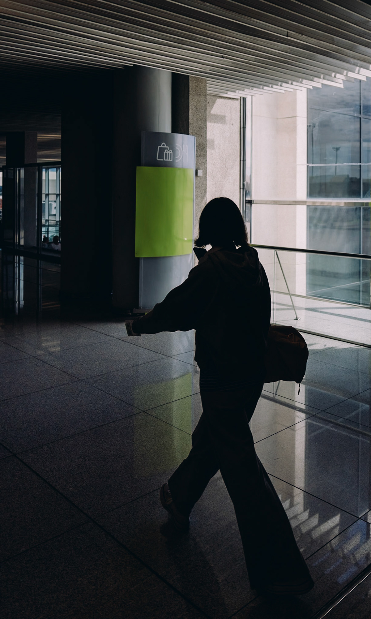 in the grand theatre of the palma de mallorca airport, a solitary figure pirouettes through the concourse, a ballet amidst the bustle. they glide past a bold splash of green, a sign that's both an accent in this composition and a marker of modernity amidst the transient crowds. their posture is one of purposeful motion, a stride that carries stories yet to be told. the light plays a delicate game, casting a geometric dance on the polished floor, reflecting the outside world in its glassy surface. there's an undercurrent of narrative in this journey, a segment of a larger voyage, each step a brushstroke in the canvas of their travels.