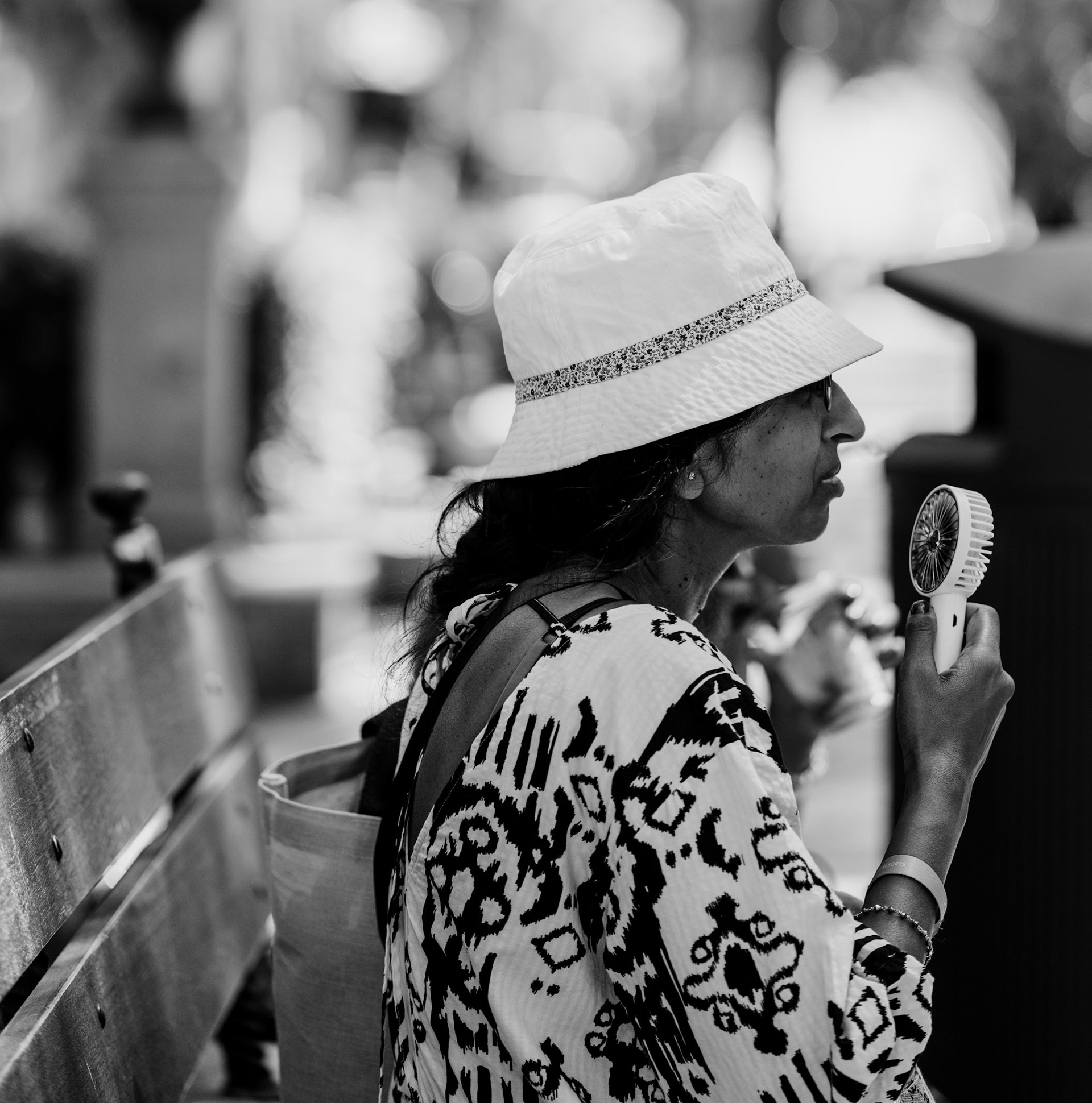 capturing the essence of summer on the elegant paseo del borne, where even in the late afternoon, the temperatures linger near 38°C. this woman, dressed in a flowing, patterned dress, finds a brief respite from the sweltering heat with a portable fan. the image reflects the resilience and resourcefulness that one develops when navigating the Mediterranean heat, all while maintaining an air of understated chic in the heart of palma.