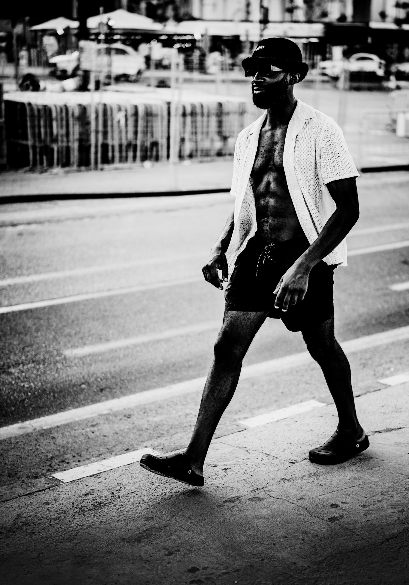 captured on the paseo marítimo in palma, this photograph exudes an air of determination and effortless style. the man's confident stride and athletic physique are accentuated by the black and white tones, drawing focus to his presence and the textures of his attire. his relaxed yet purposeful walk against the backdrop of the bustling promenade tells a story of self-assuredness and individuality, making him a striking subject amid the city's vibrant energy.