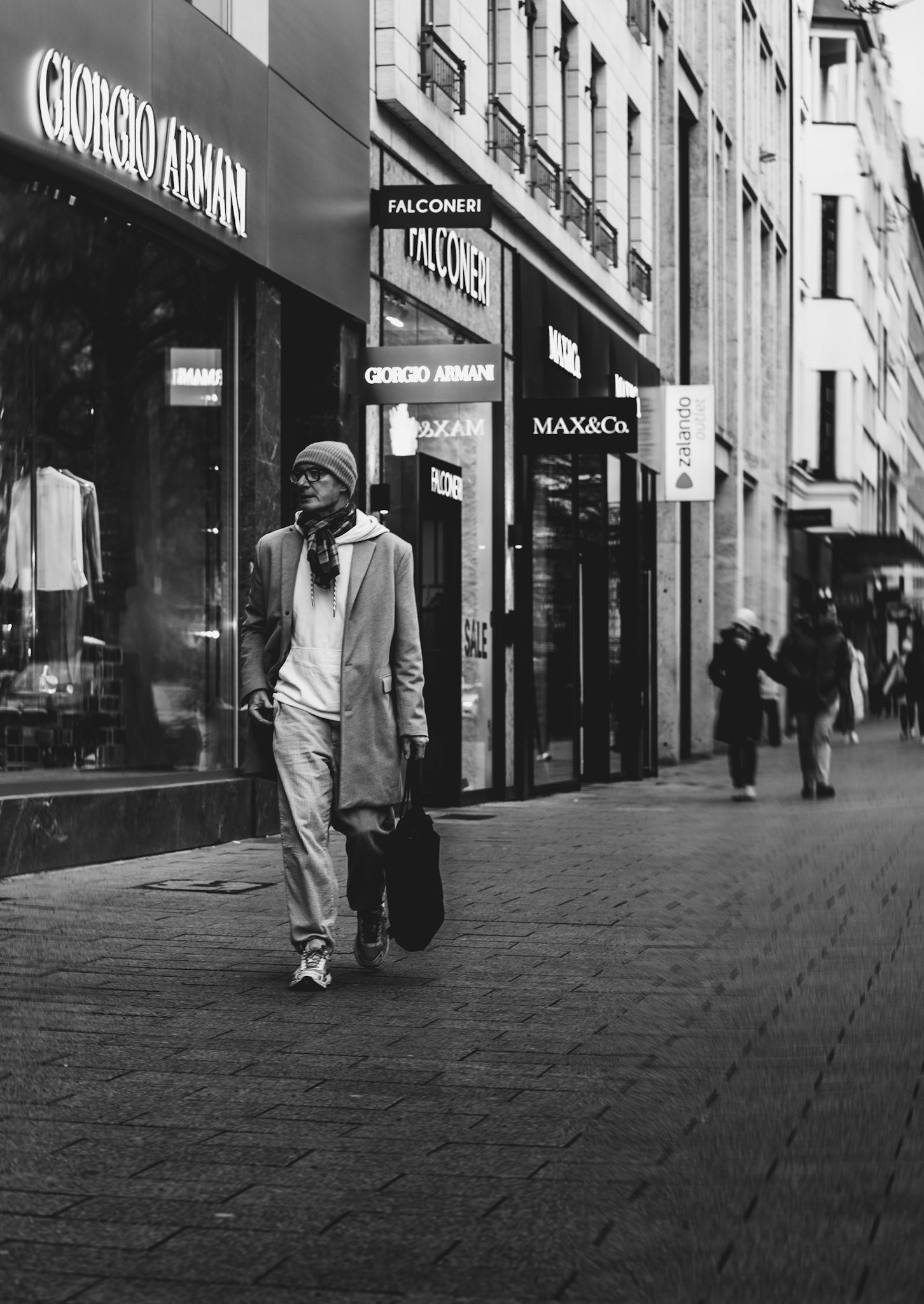 on königsallee in düsseldorf, amidst the grandeur of flagship fashion stores, an elegantly dressed man strides with purpose. his outfit, a blend of casual sophistication, complements the luxurious backdrop. he carries the air of the avenue with him, a perfect fit in this high-fashion tableau on a clear day.