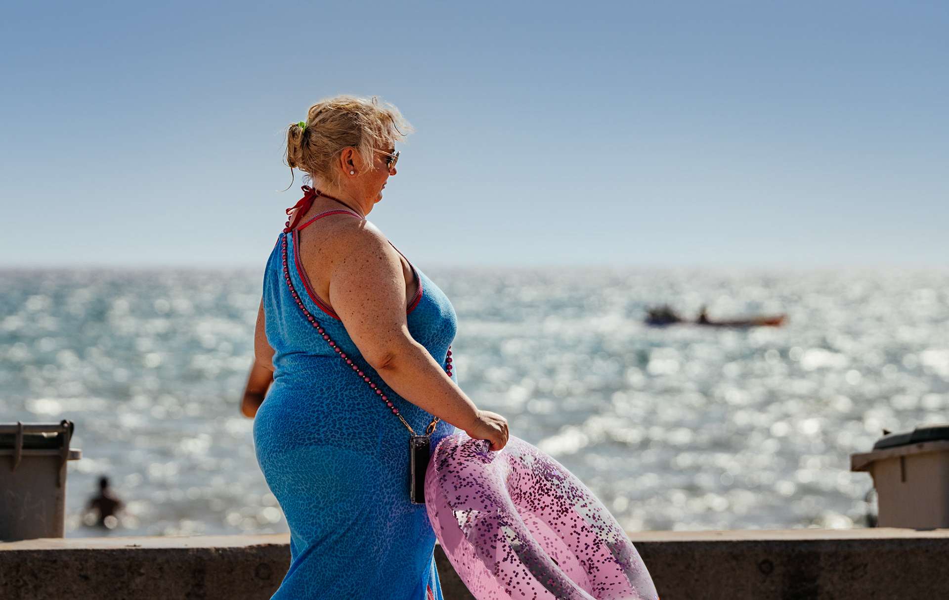 during a late afternoon walk in el arenal, i captured this vibrant scene of a woman by the seaside. her blue dress and the pink inflatable toy in her hand contrast beautifully against the glistening ocean backdrop. the sun casts a warm glow, highlighting the textures and colors, and creating a serene and joyful summer atmosphere. this photograph celebrates the simple pleasures of a beach day, encapsulating the essence of leisure and the carefree spirit of coastal life.