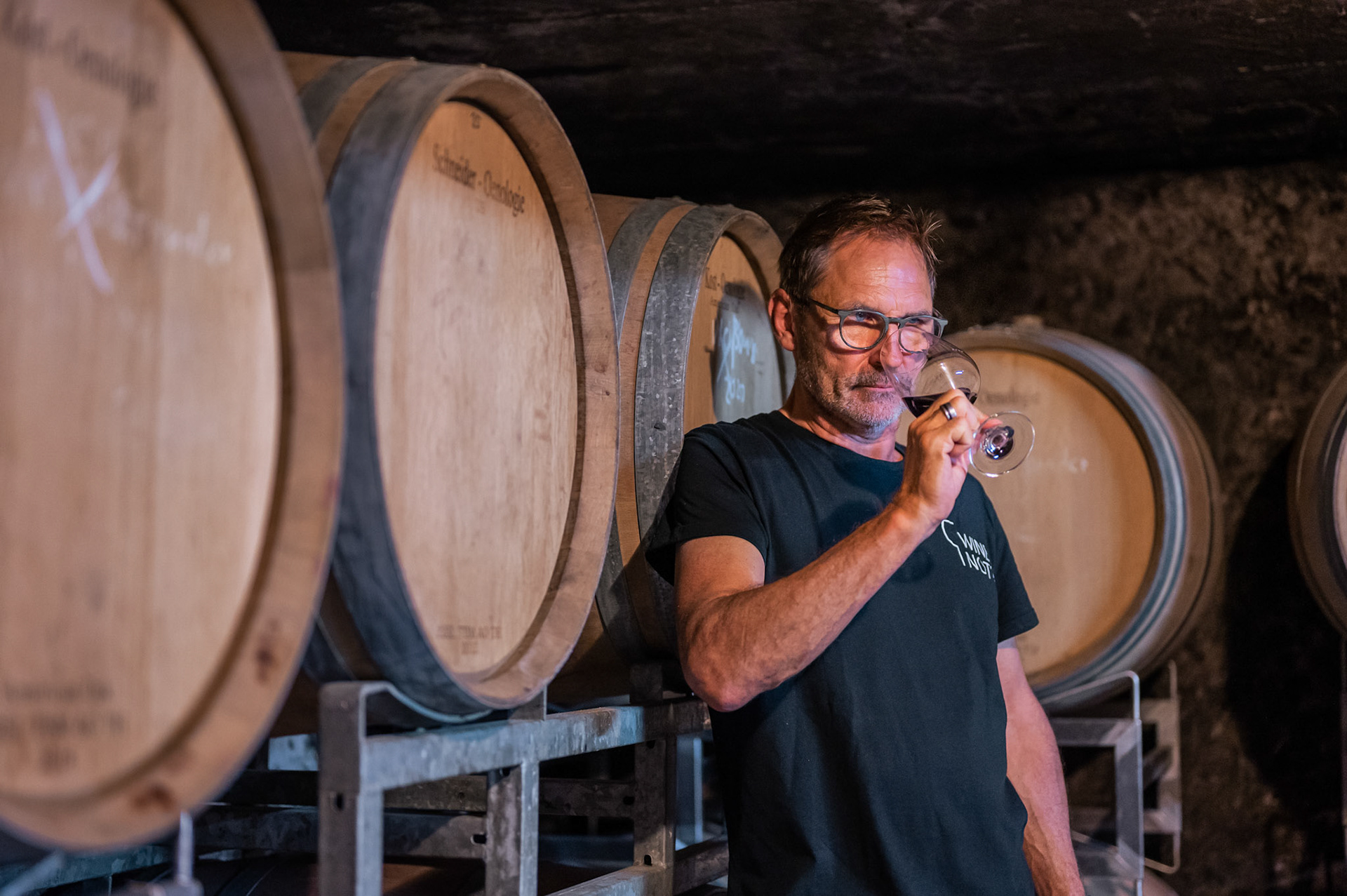 Mann riecht an einem Glas Wein im Weinkeller mit Weinfässer im Hintergrund