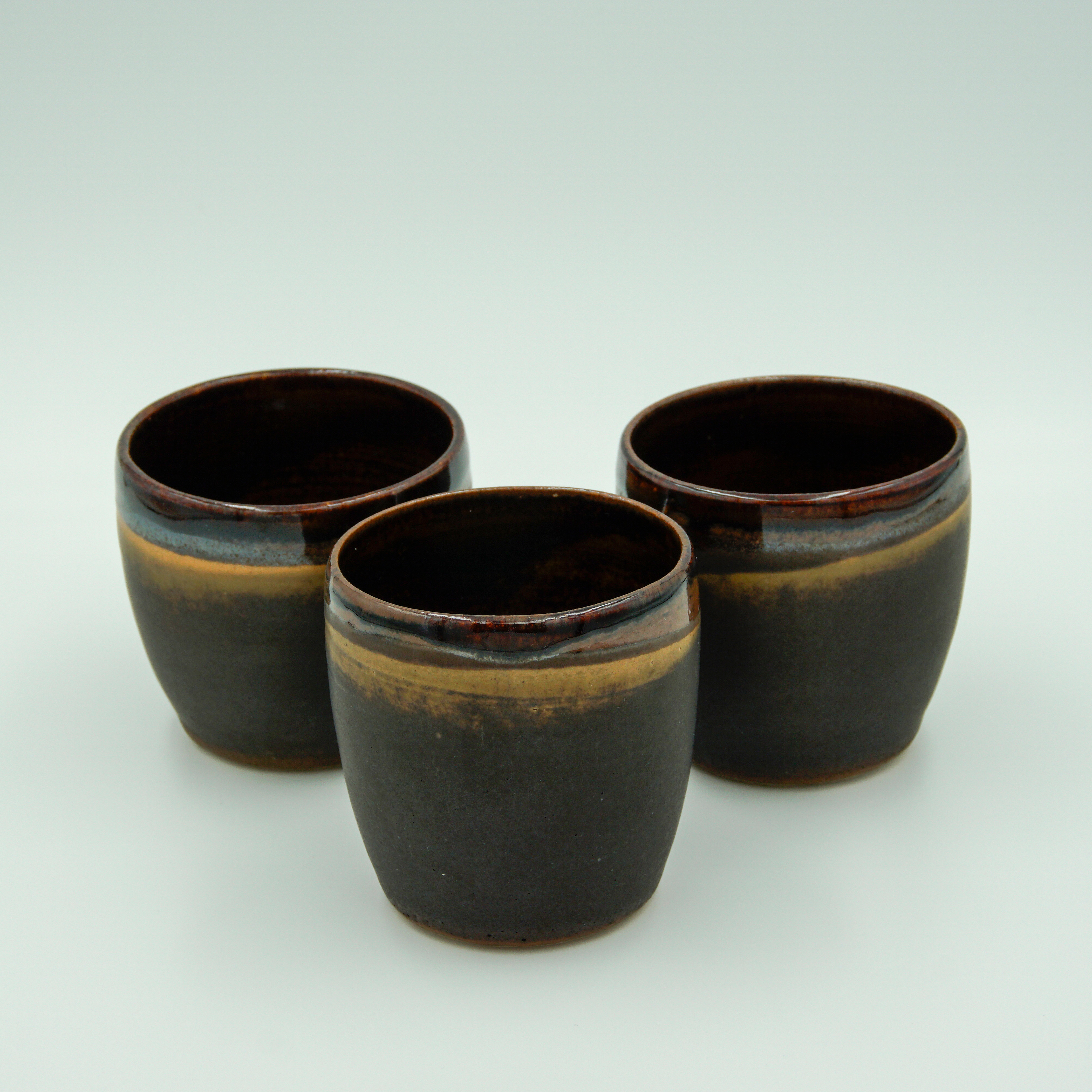 Three beakers in tenmoku and matt black/orange glazes