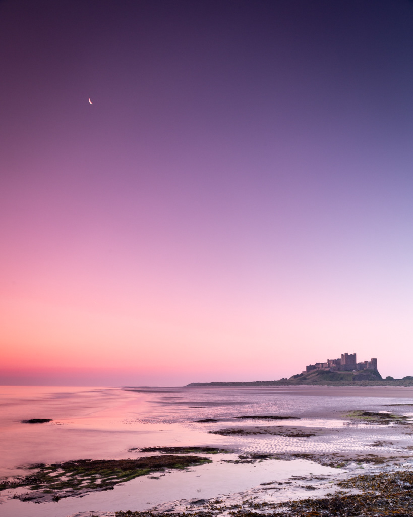Bamburgh Castle in Pre-dawn light overlooked by the moon