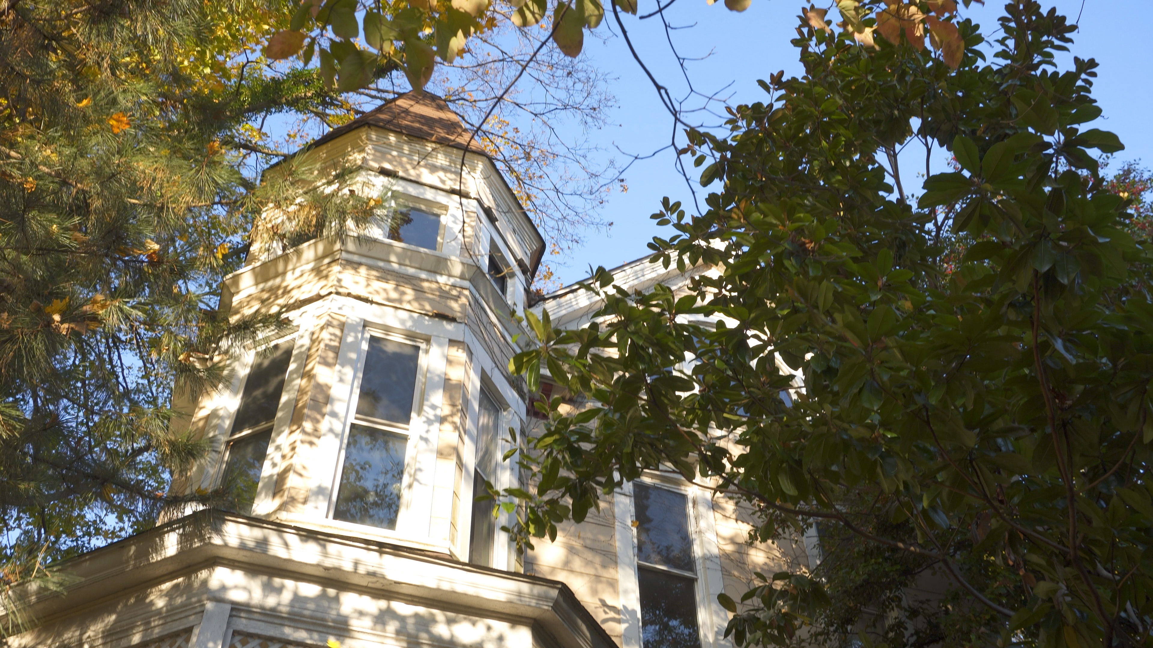 Peeking through the trees at the third floor cuppola of a 120+ year old Victorian home