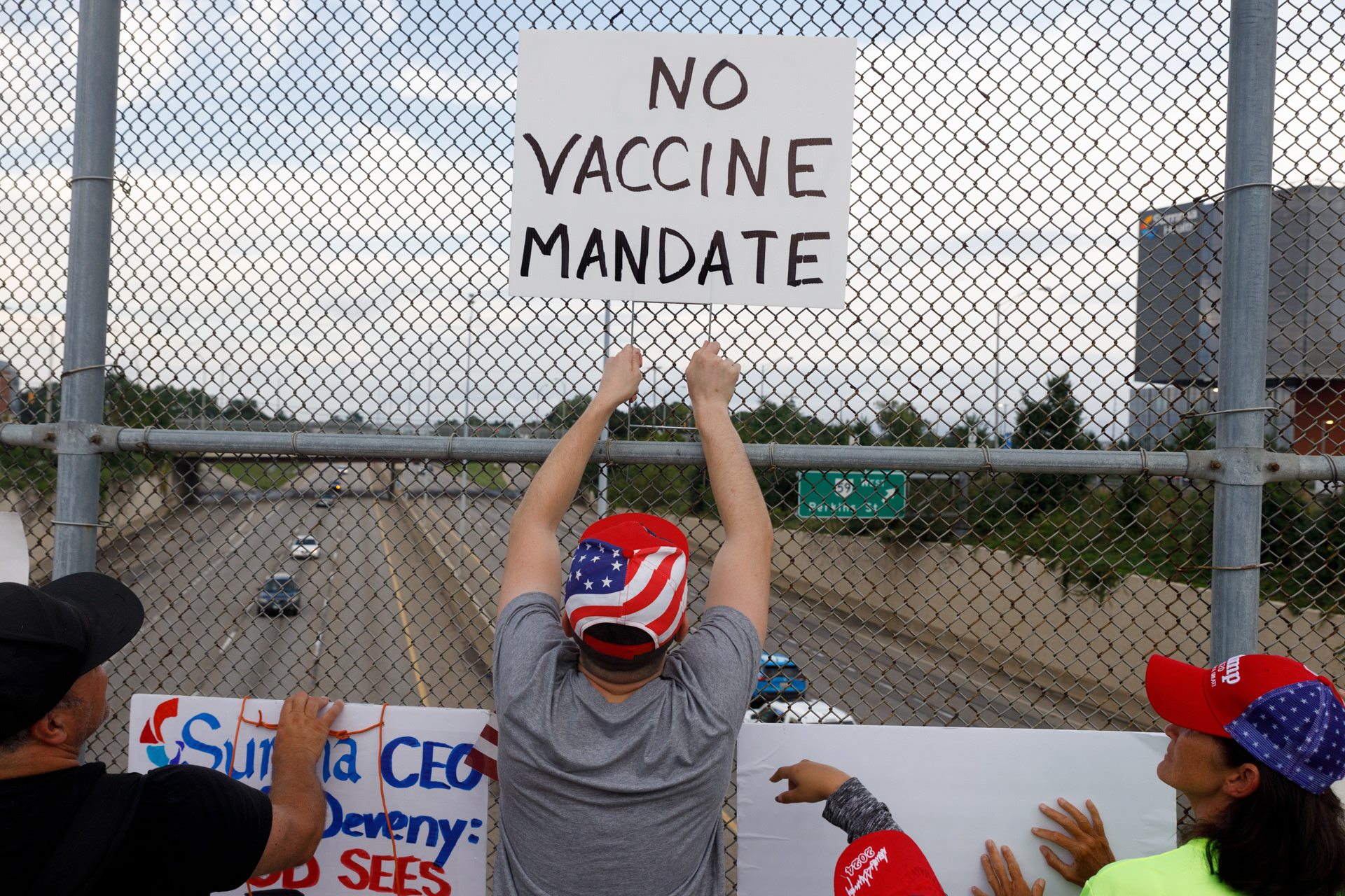 Young man raises sign to protest against coronavirus disease (COVID-19) vaccine mandates at Summa Health Hospital in Akron, Ohio, U.S., August 16, 2021. Protesters pushed their signs up against the chain linked fence to show drivers on Ohio State Route 8.