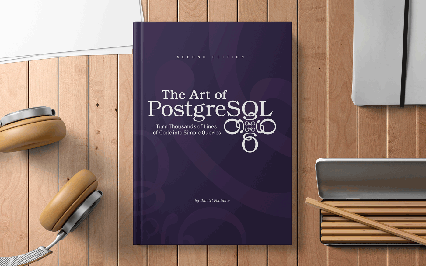 Hardcover book on a wooden desk with headphones, pencils, and paper