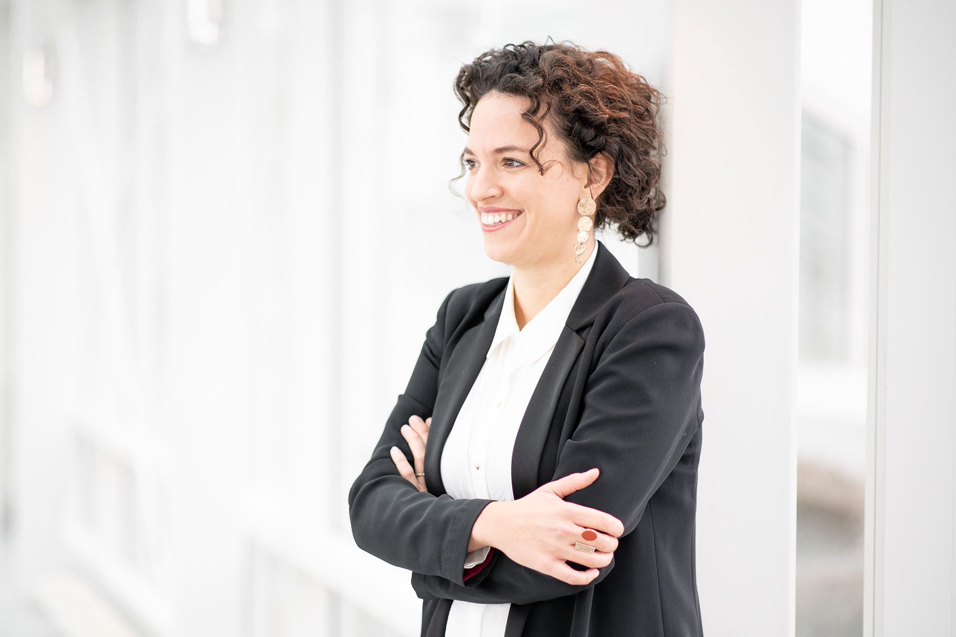 Bewerbungsfotos einer Frau, die sympathisch lachend mit verschränkten Armen an einer weißen Säule steht