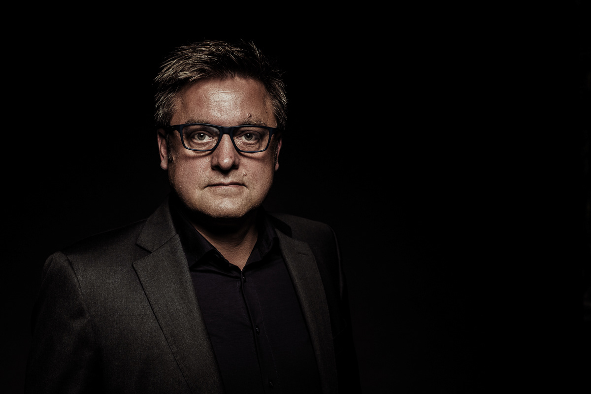 Mitarbeiterportrait Christoph Gabler, Portrait des Geschäftsführers einer Rechtsanwaltskanzlei vor schwarzem Hintergrund im Fotostudio Christoph Gabler, mit gezielter Beleuchtung des Oberkörpers