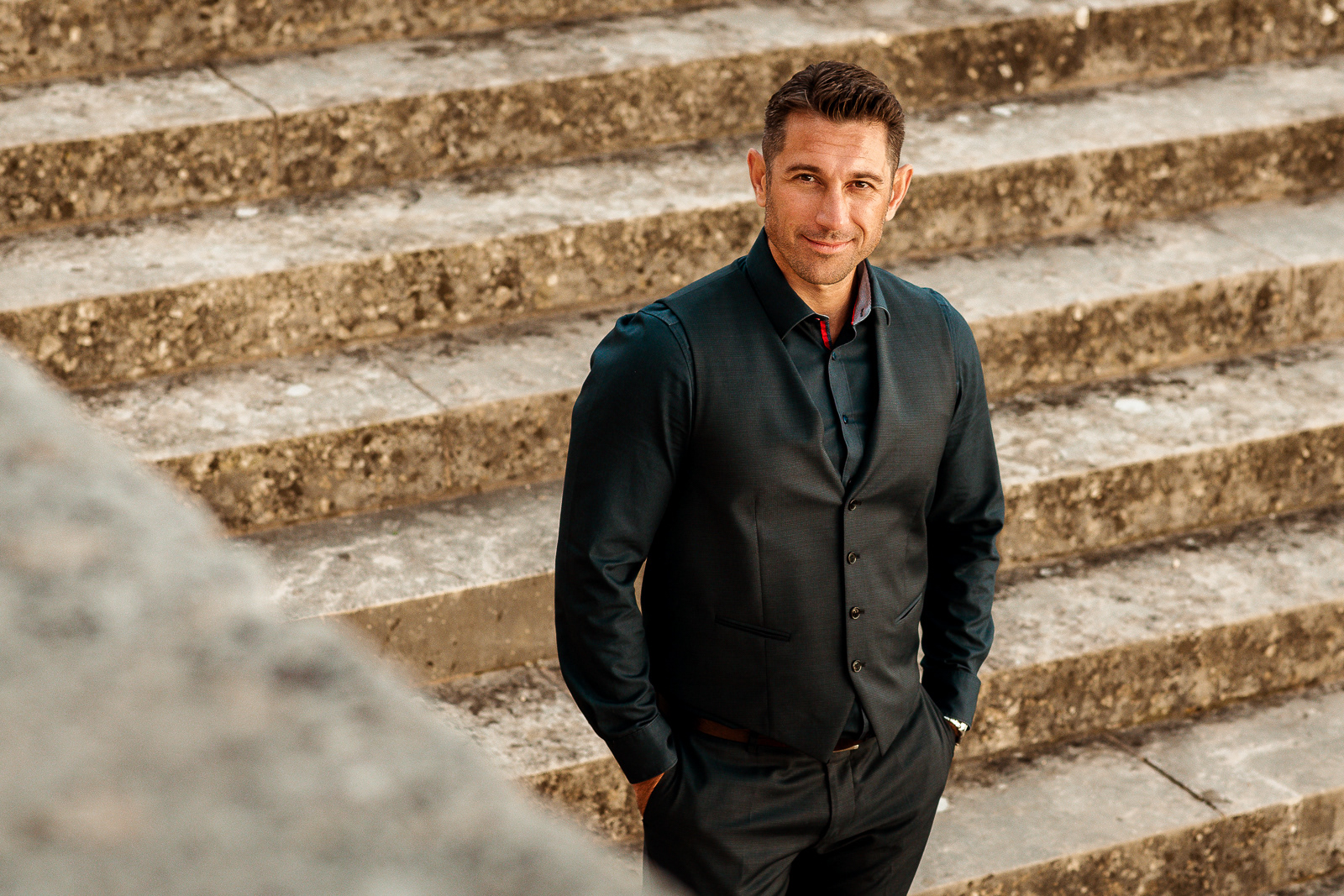 Businessportrait Gabler Foto, stilvoll gekleideter Mann läuft bei Sonnenuntergang ein große Steintreppe hinunter und lächelt in die Kamera