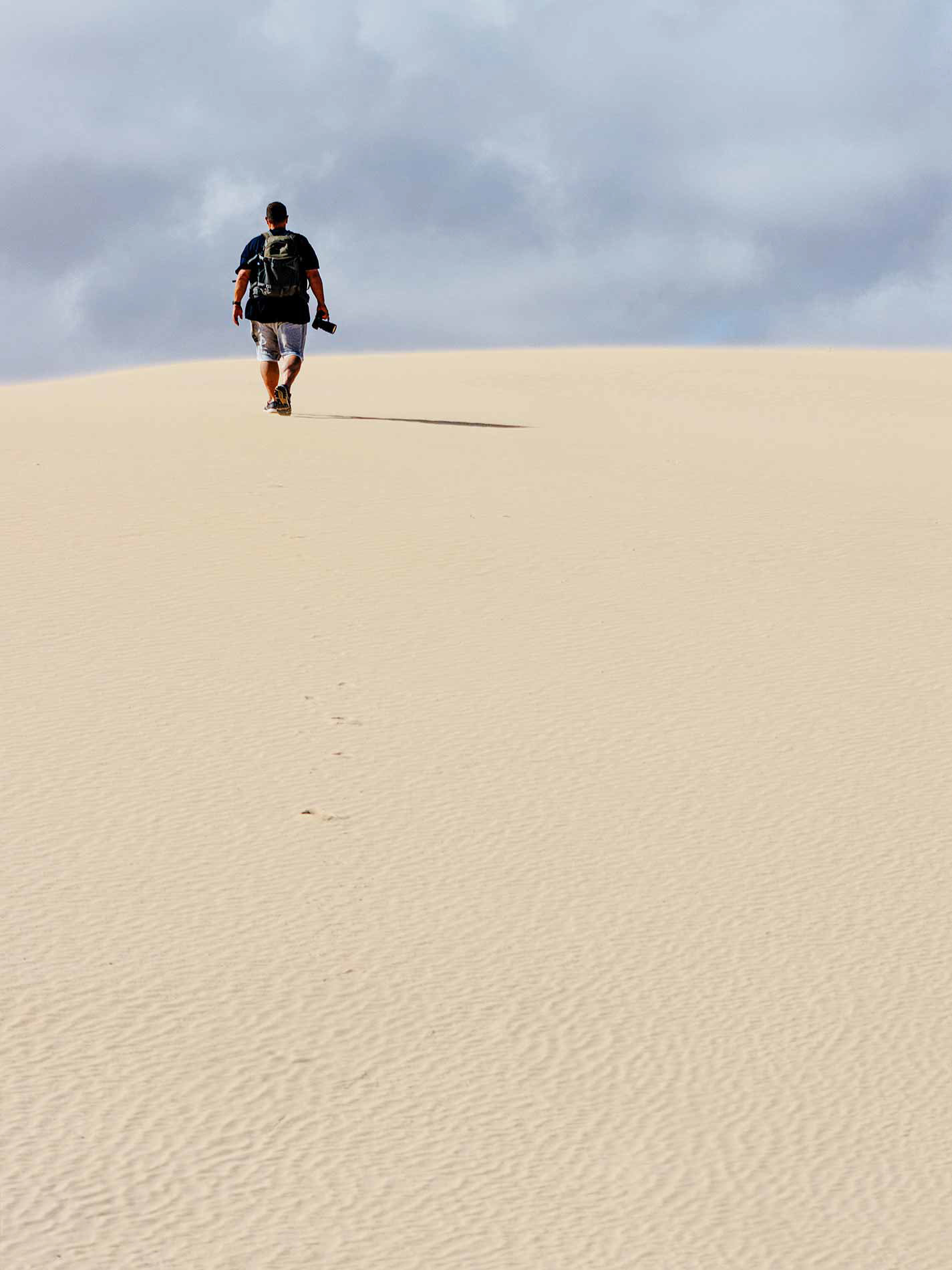 Helmuth geht mit der Kamera eine Sanddüne hinauf.