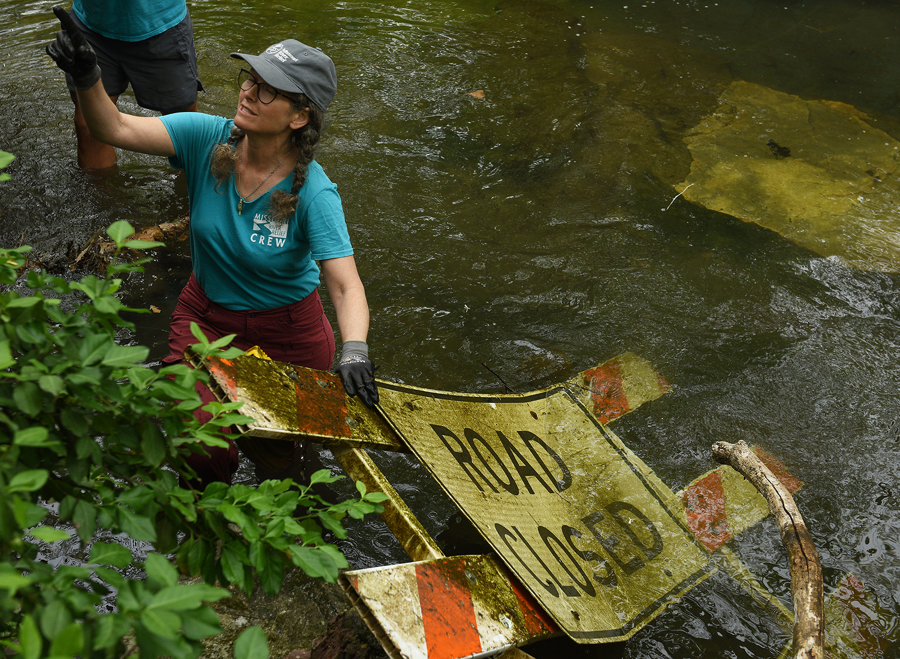 Laura Semken works to lift a large sign out of Flat Branch Creek on Wednesday at the MKT Nature and Fitness Trail in Columbia. Semken, a member of the Missouri River Relief crew, said the creek is “near and dear to my heart.” She has been helping maintain the area since moving to Columbia in 2019.