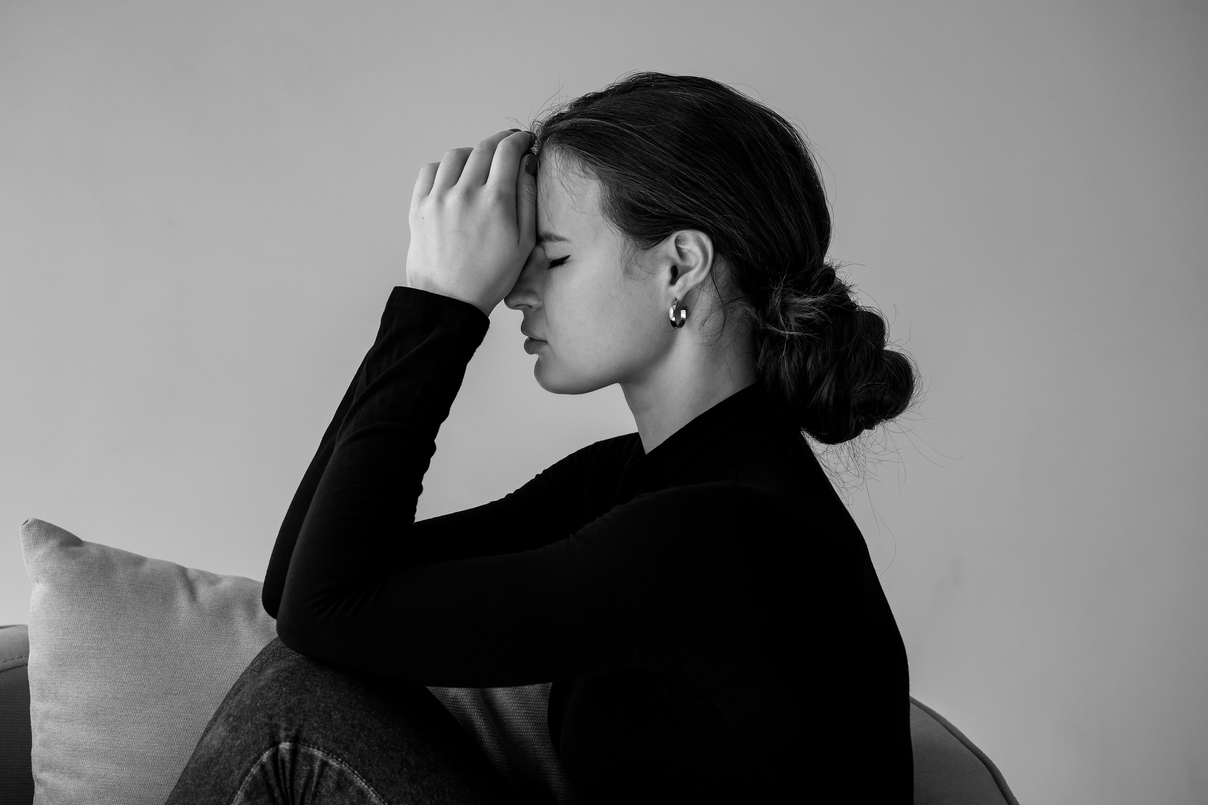 A woman holds her arms in front of her face and has her eyes closed. Sad expression.